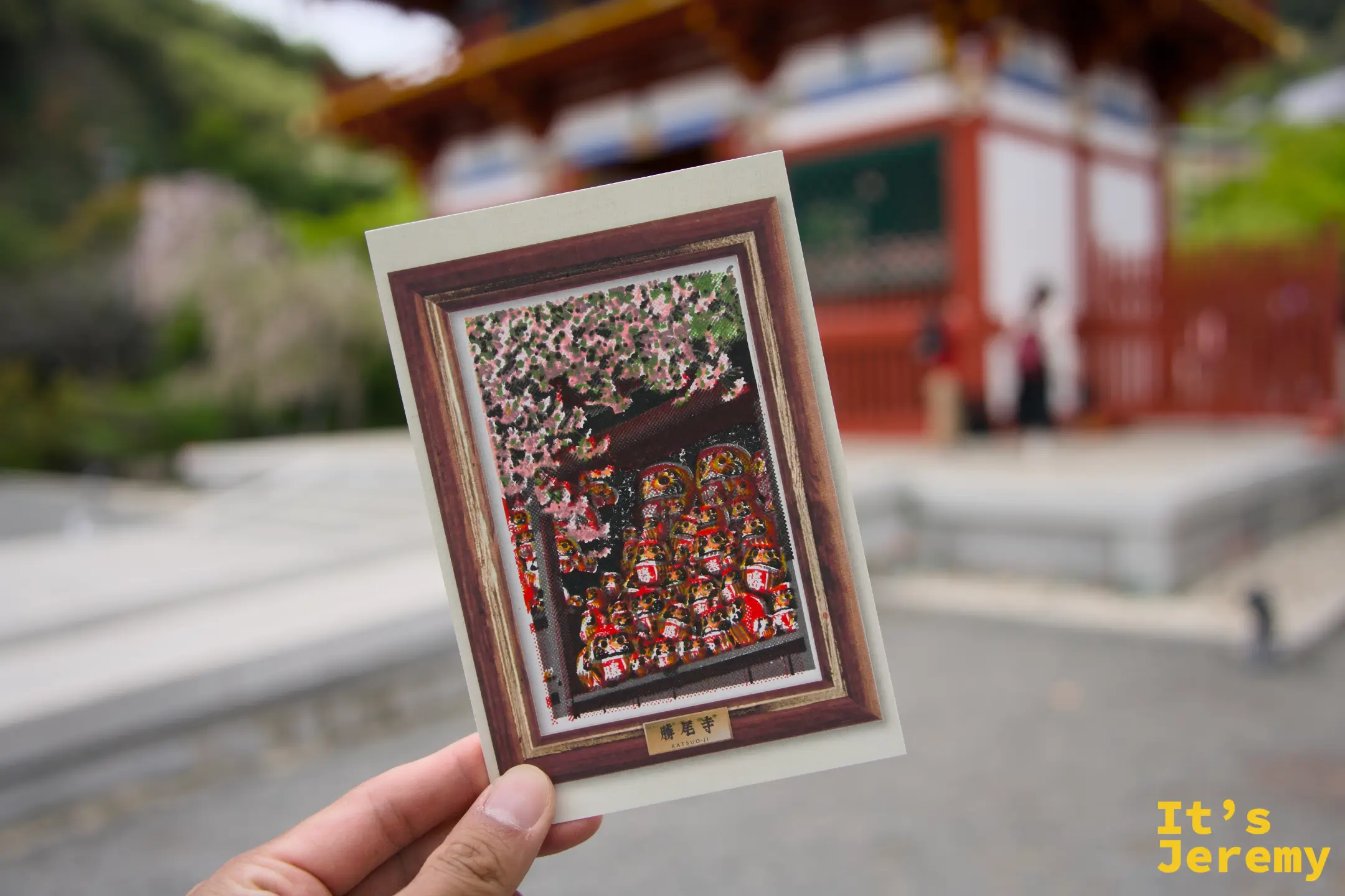 手持完成版明信片，背景是勝尾寺山門