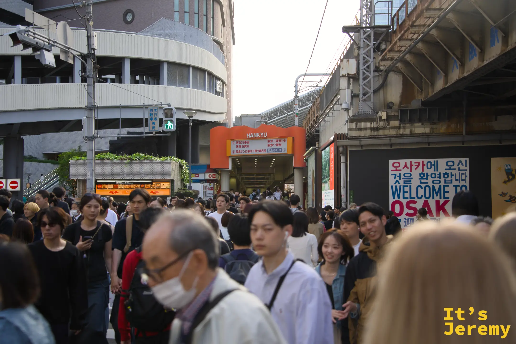 梅田阪急百貨前的人潮，背景 WELCOME TO OSAKA 看板清楚可見，傍晚的下班流把整條街道填滿