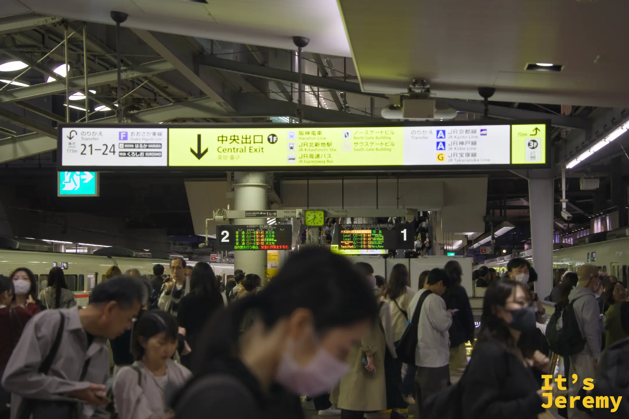JR 大阪站月台，中央出口的黃色大型指示看板懸在頭頂，入夜的月台依然擠滿人