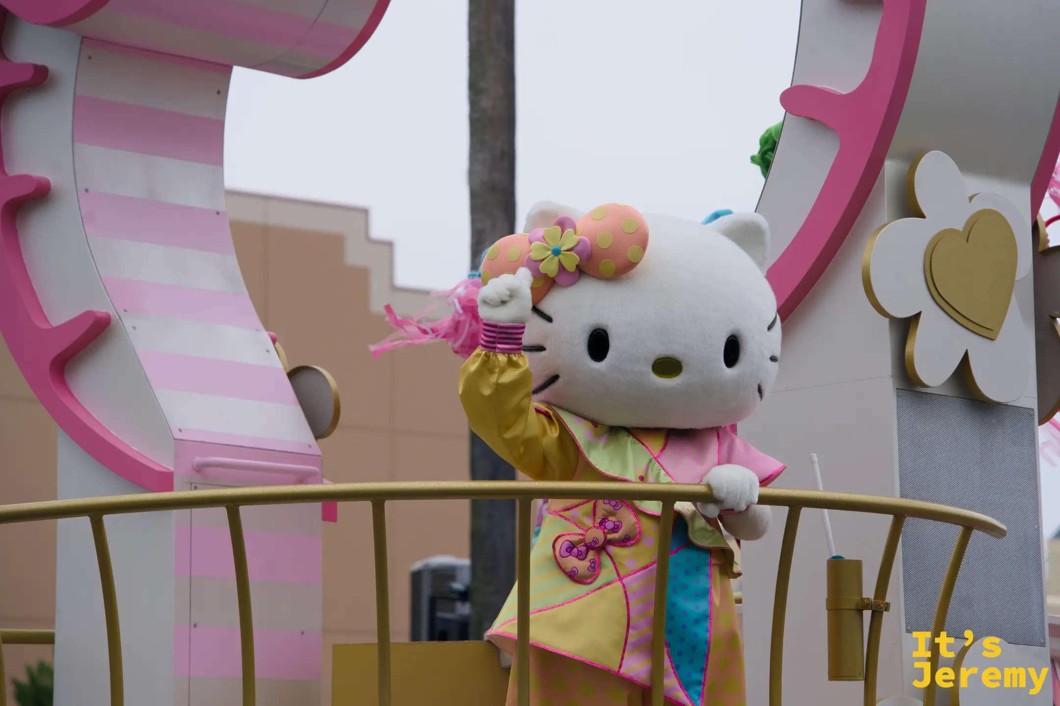 Hello Kitty 站在花車上揮手，黃色和服配上花朵頭飾，是一個很少見的特別造型