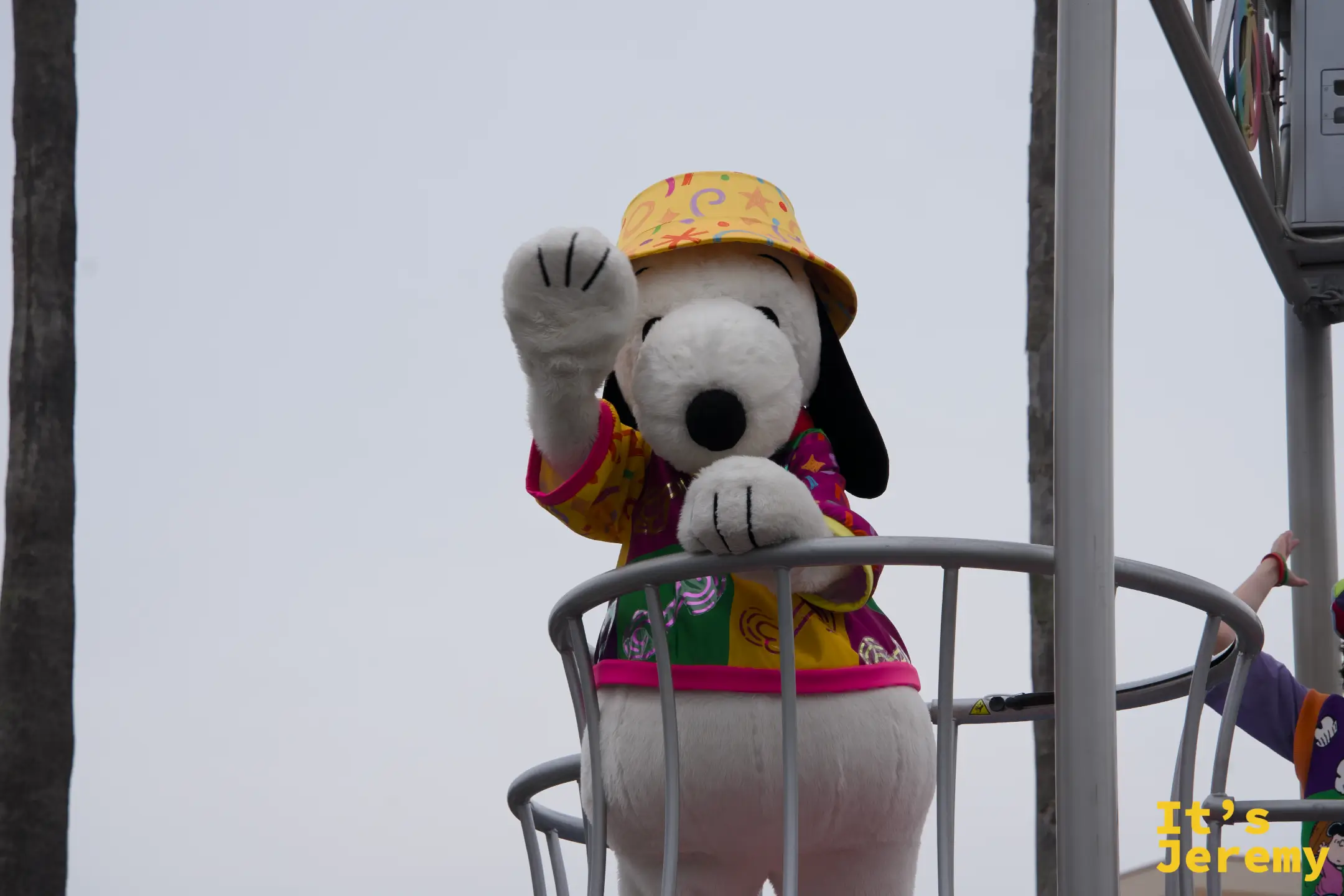 Snoopy 站在高處向觀眾揮手，身穿黃色橘色夏威夷衫，搭配黃色水桶帽