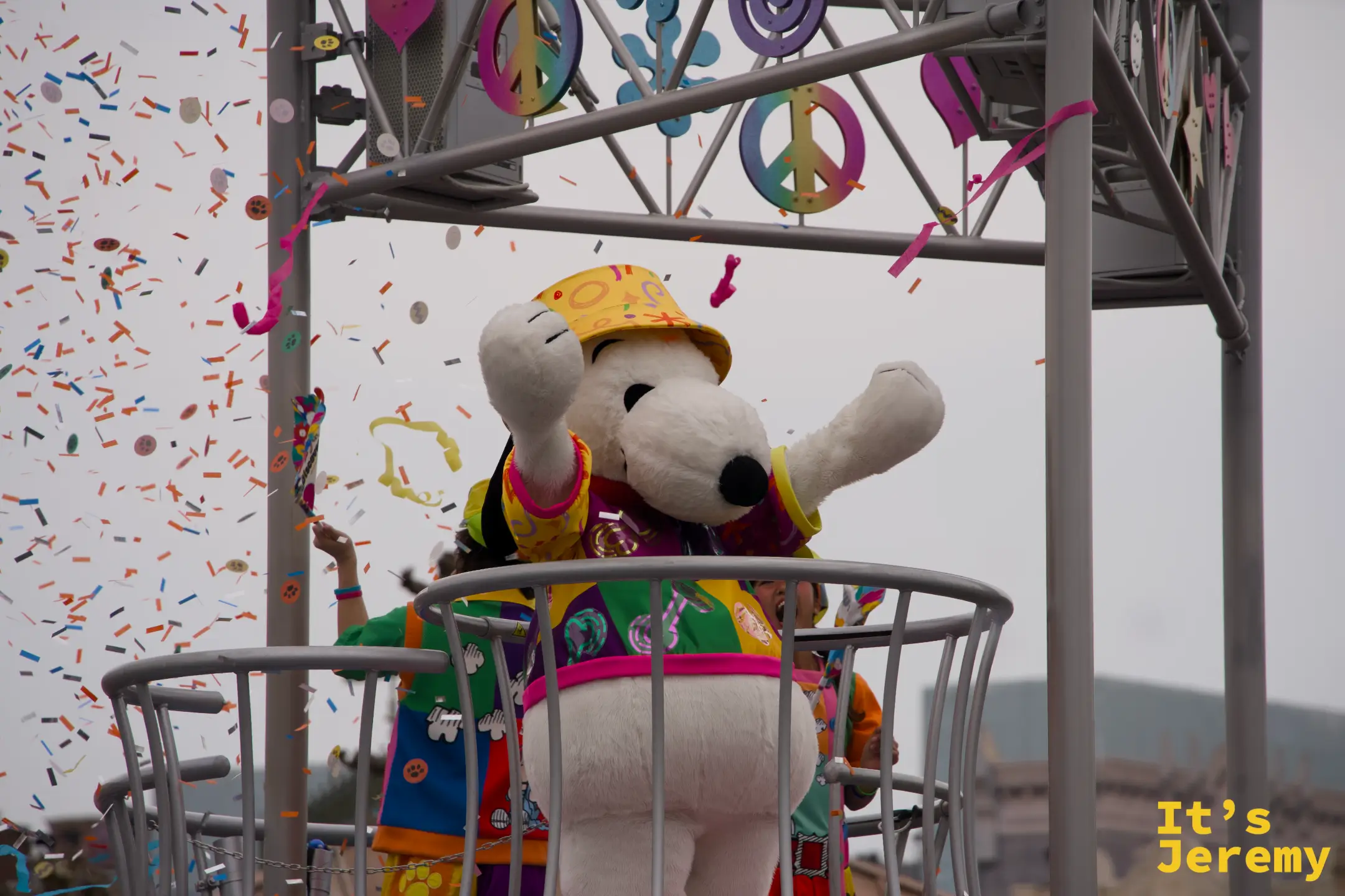 Snoopy 在彩帶飛舞中揮舞雙手，背景是五顏六色的和平符號裝飾