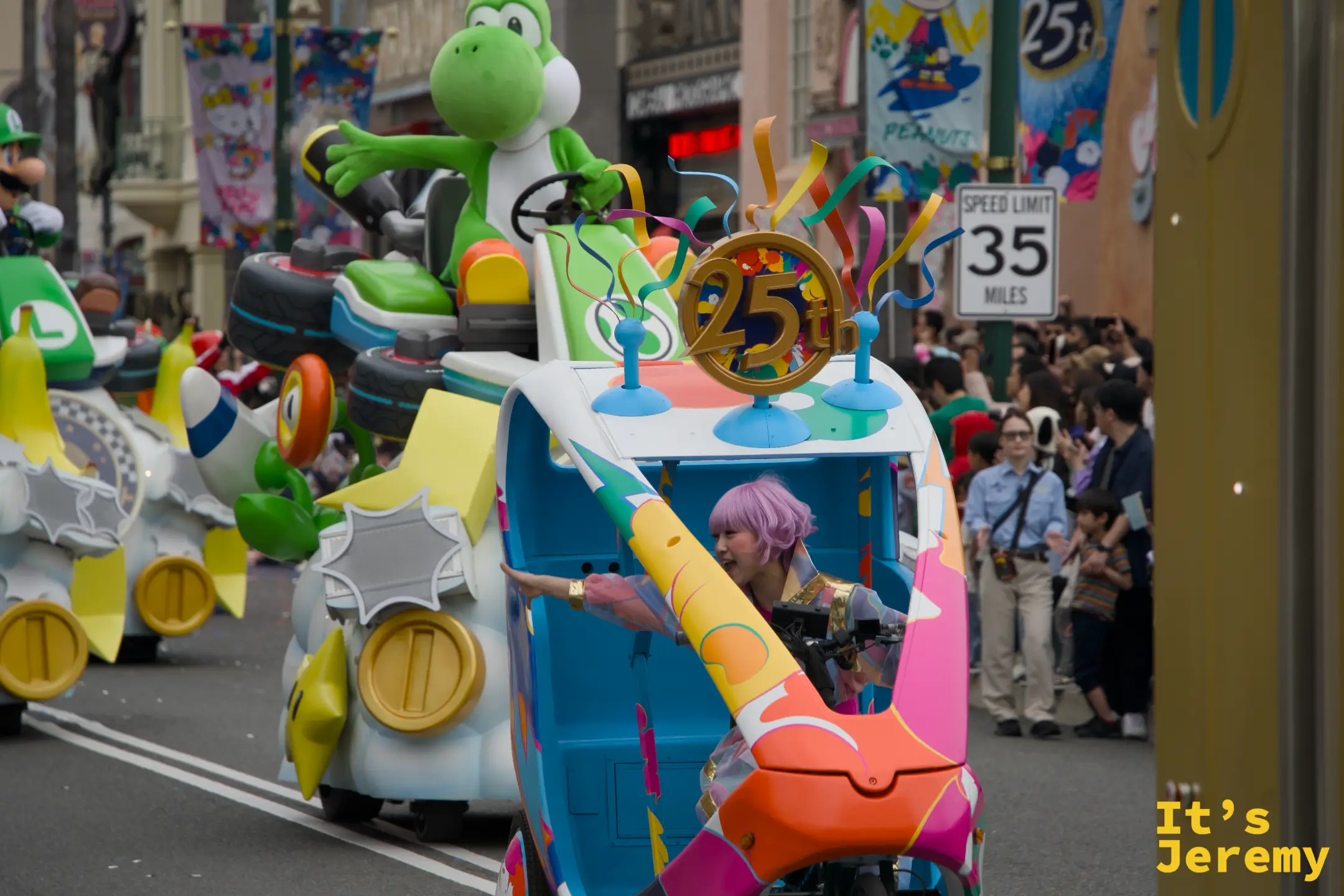 Mario Kart 花車全景，Yoshi 駕著綠色賽車在前，25th 金色標誌懸掛花車頂部，觀眾沿著街道排成人牆
