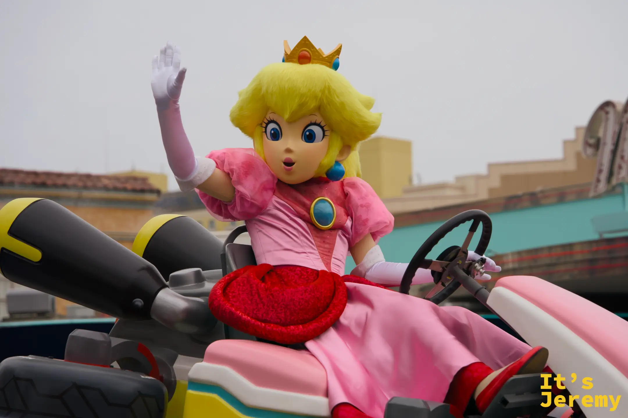 Princess Peach 特寫，粉色蓬裙、白色手套、金色皇冠，一手揮向觀眾，神情既優雅又生動