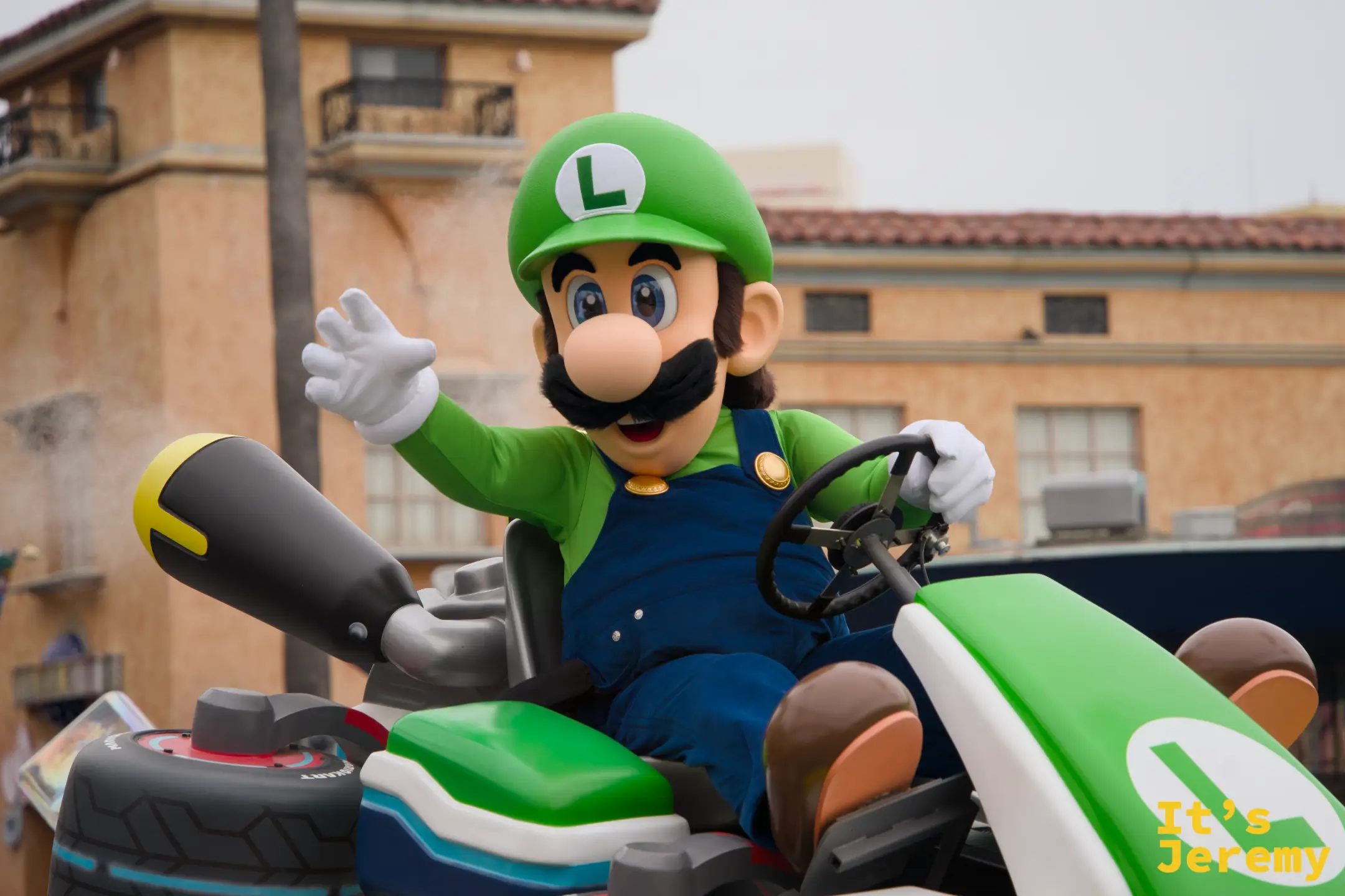Luigi 特寫，L 字賽車裡的 Luigi 對著攝影機揮手，後方的 Mel