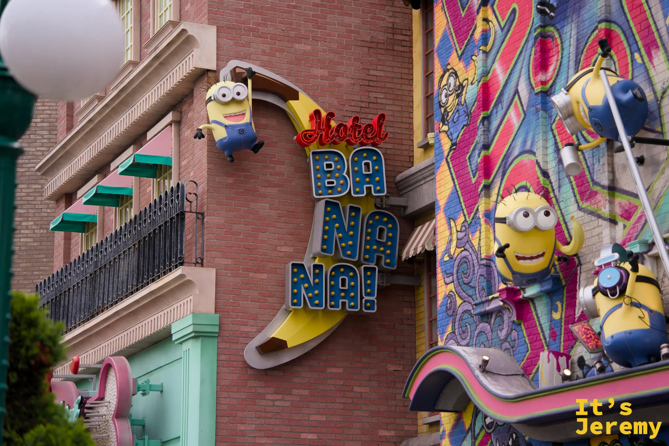 「Hotel Banana」霓虹招牌，一隻 Minion 掛在香蕉形狀的招牌上，整面建築牆上都是 Minion 的插畫