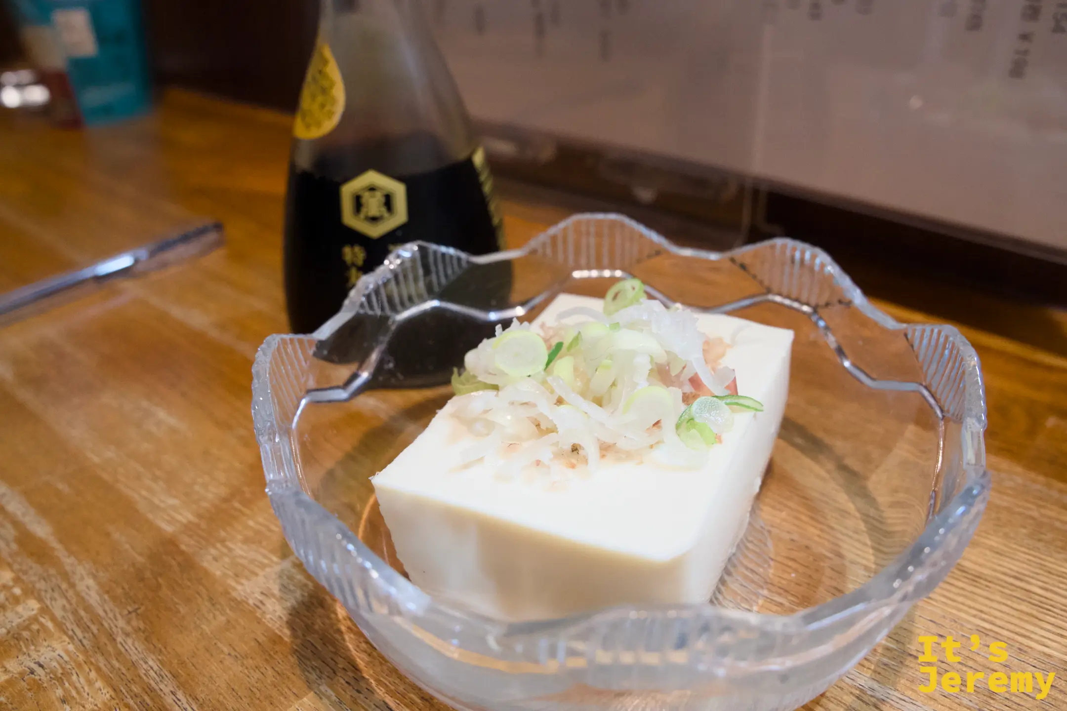 冷やっこ：豆腐鋪上柴魚花與蔥花，旁邊放著一瓶日本酒