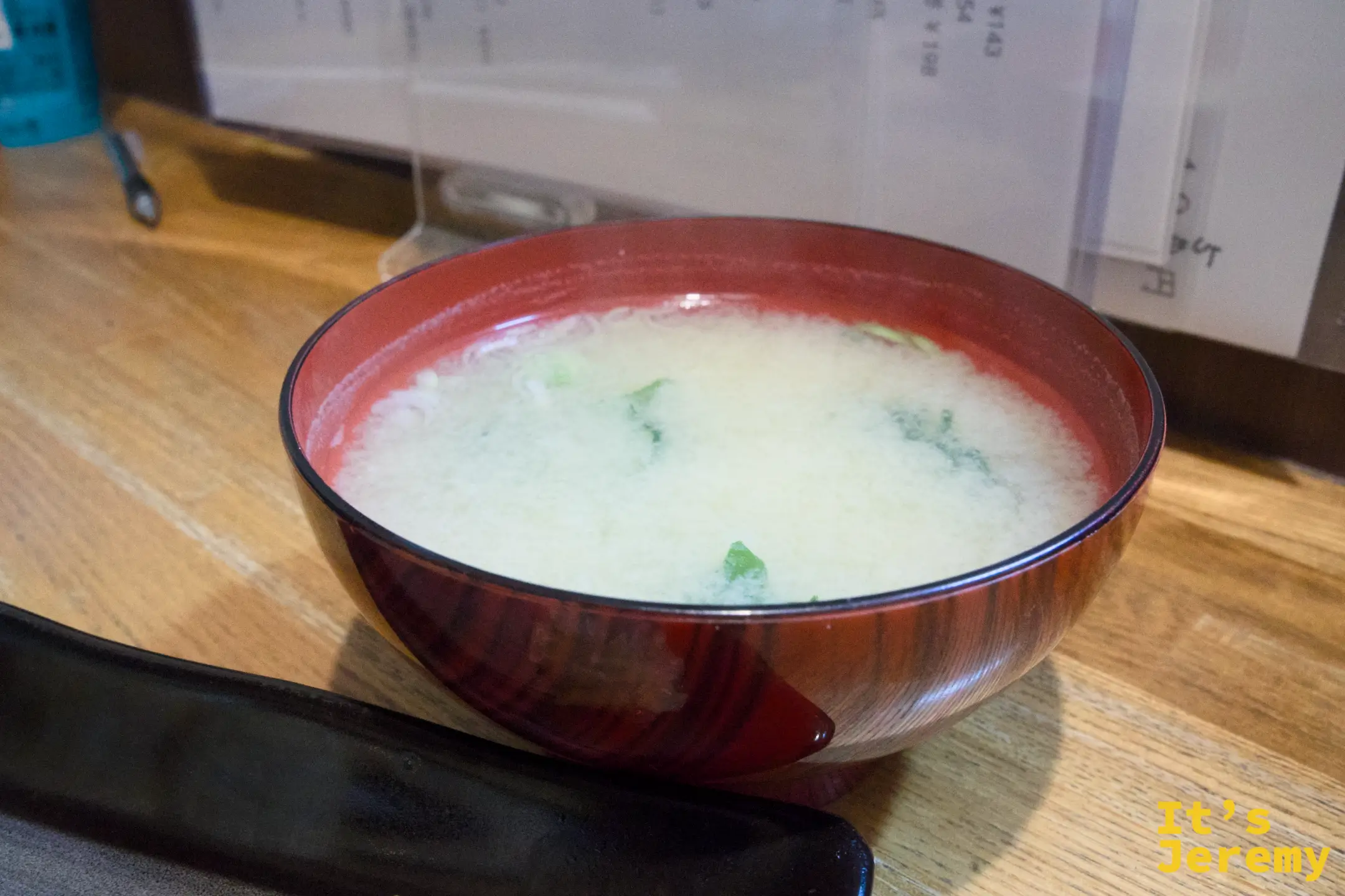 味噌湯盛在紅漆碗裡，白色湯面點綴著蔥花