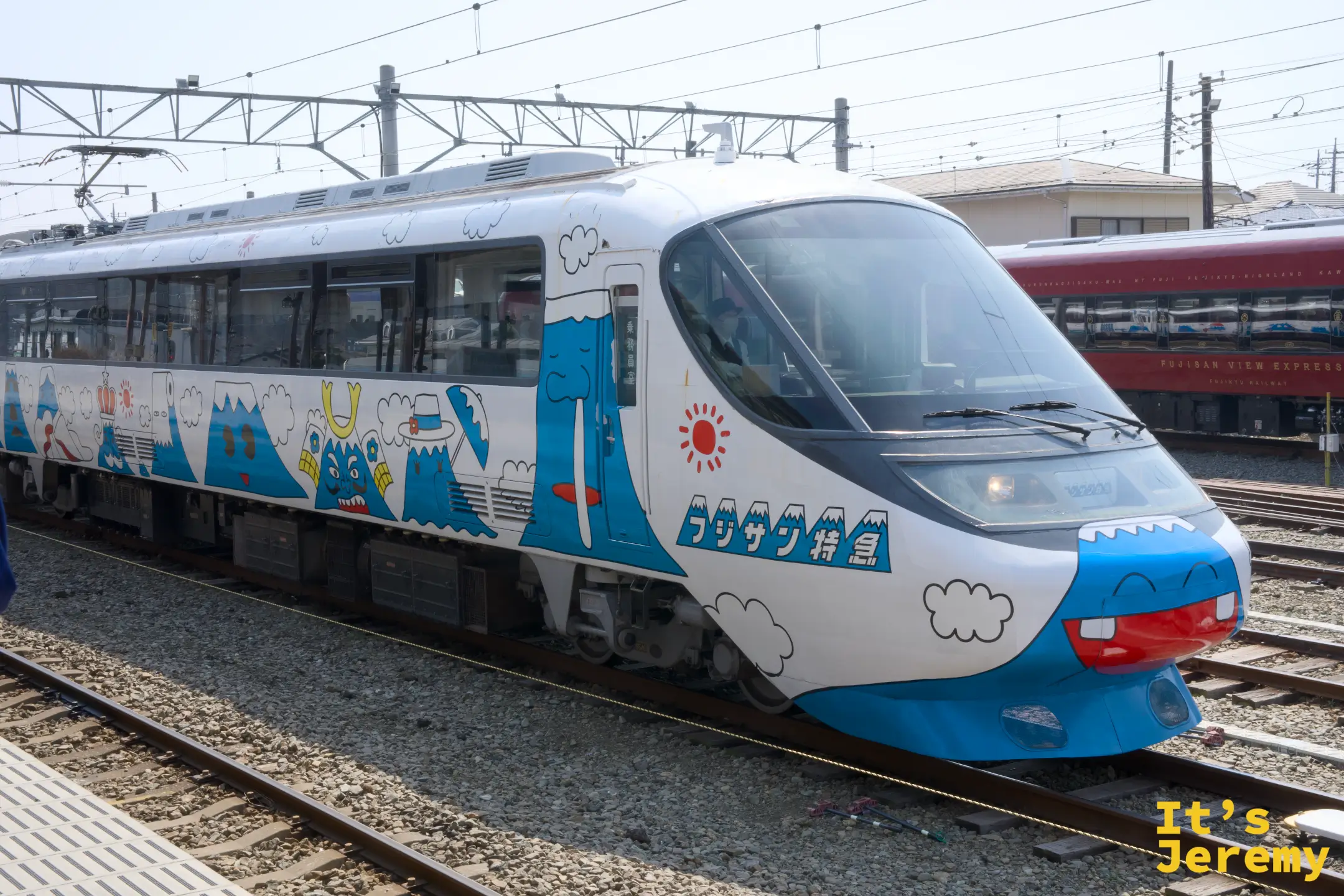 停在月台的富士急行「フジサン特急」列車，藍色車身印著卡通富士山、雲朵與微笑山峰