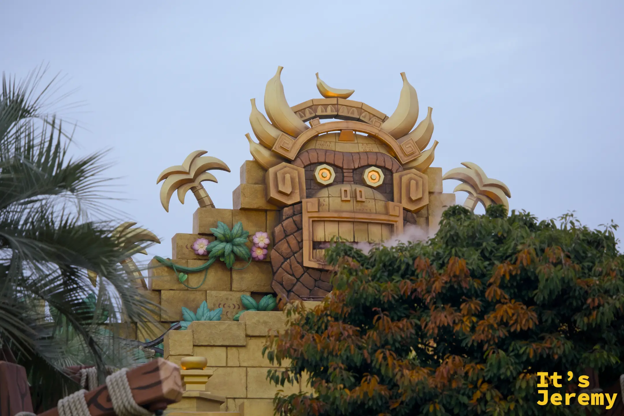 Tiki Tong 神像建築，從棕櫚樹葉隙間望去，橘色眼珠搭配香蕉圖騰的石雕建築令人印象深刻