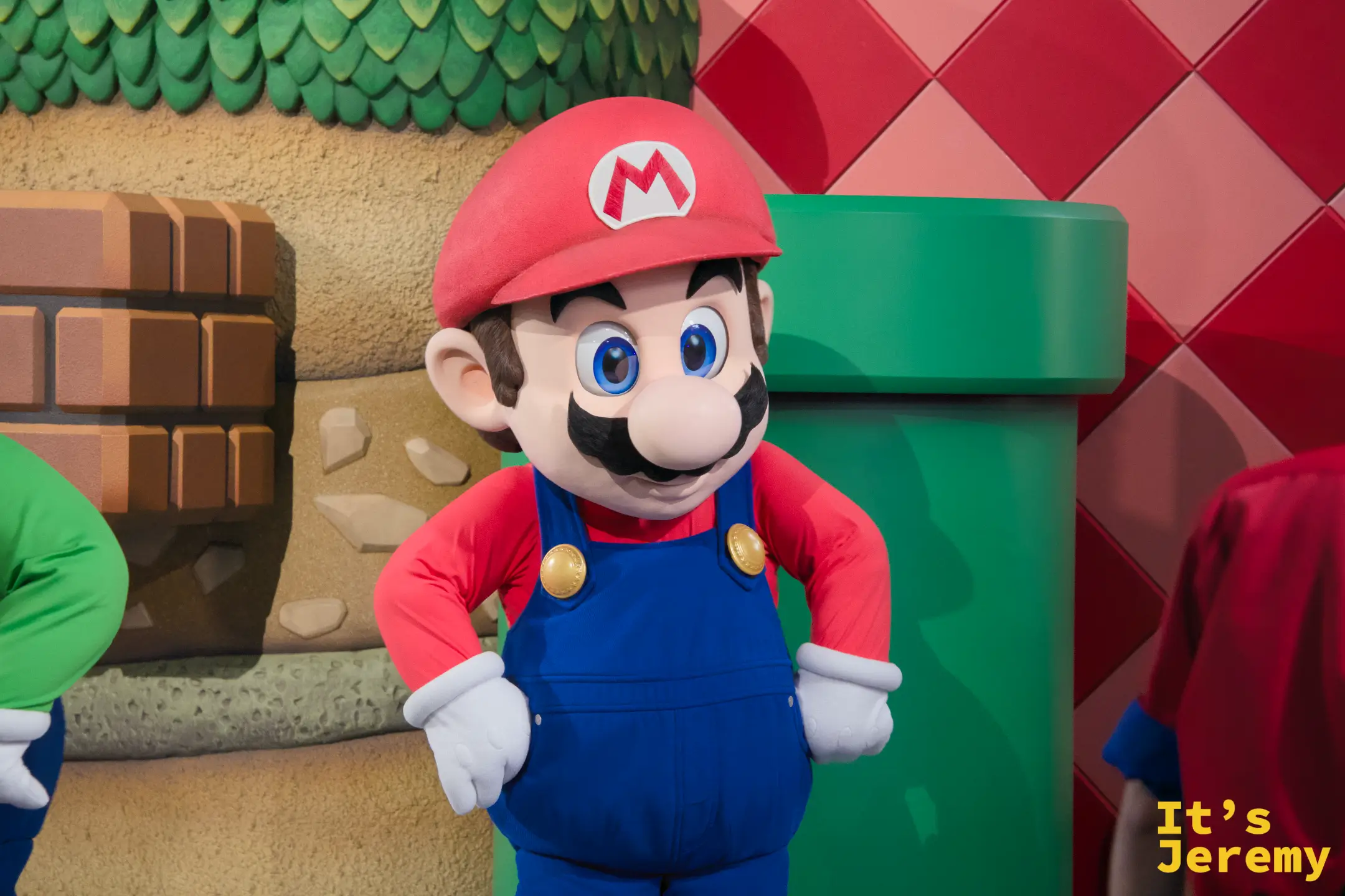 Mario 本人出現了！與遊客互動的 Mario 角色，面對鏡頭時眼神充滿活力，綠色水管背景配色剛好