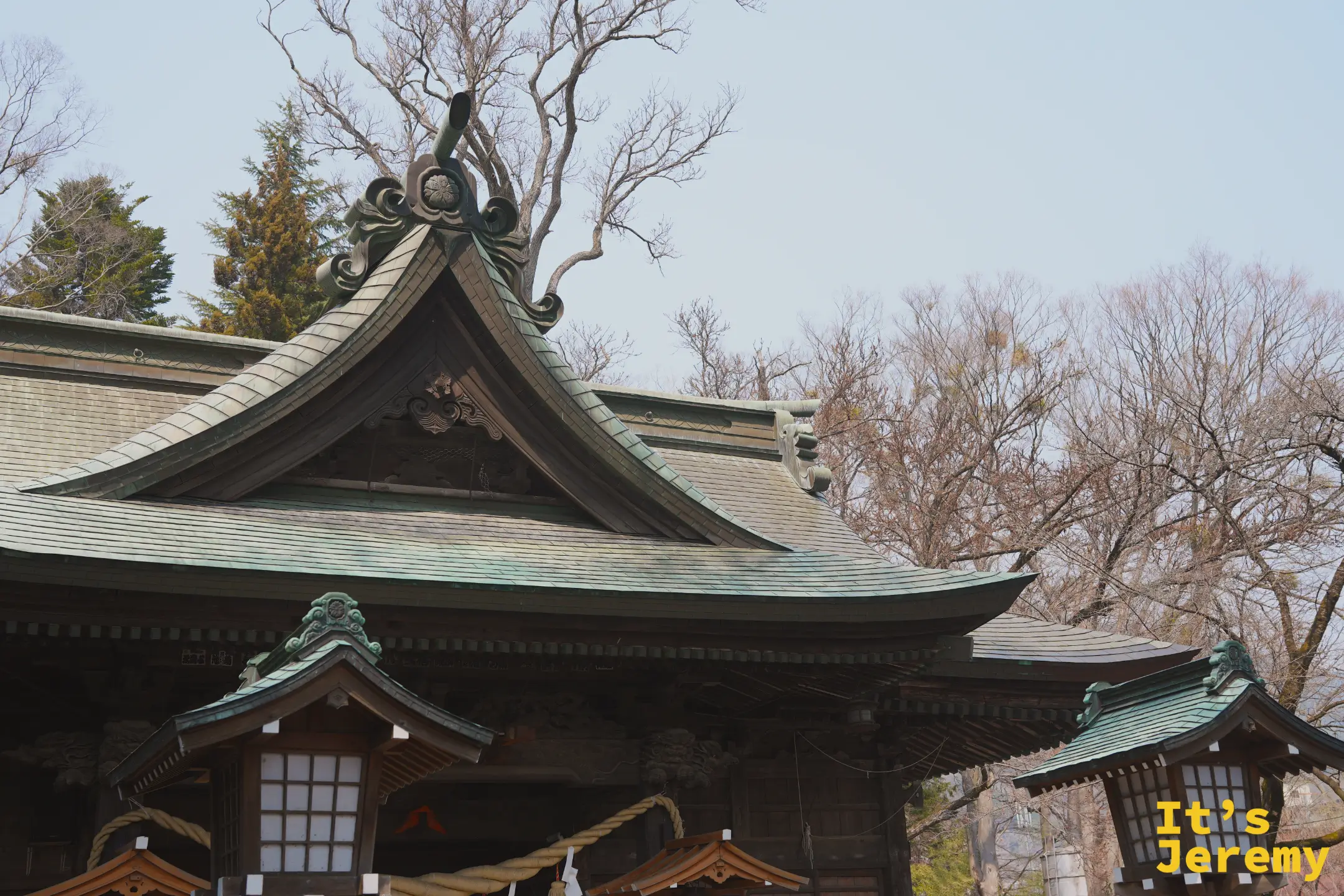 冨士山下宮小室浅間神社的主殿，青銅色屋瓦與精雕的博風板，周圍是落葉樹