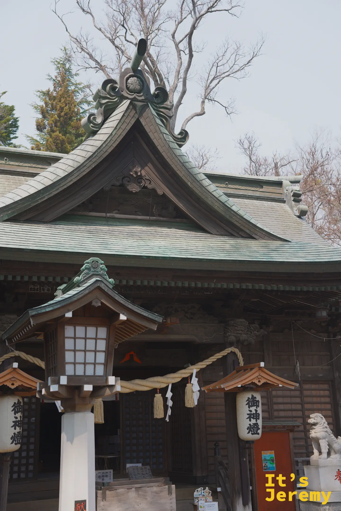 神社拜殿入口的注連繩橫跨白色柱子，柱上掛著寫有「御神燈」的紙燈籠