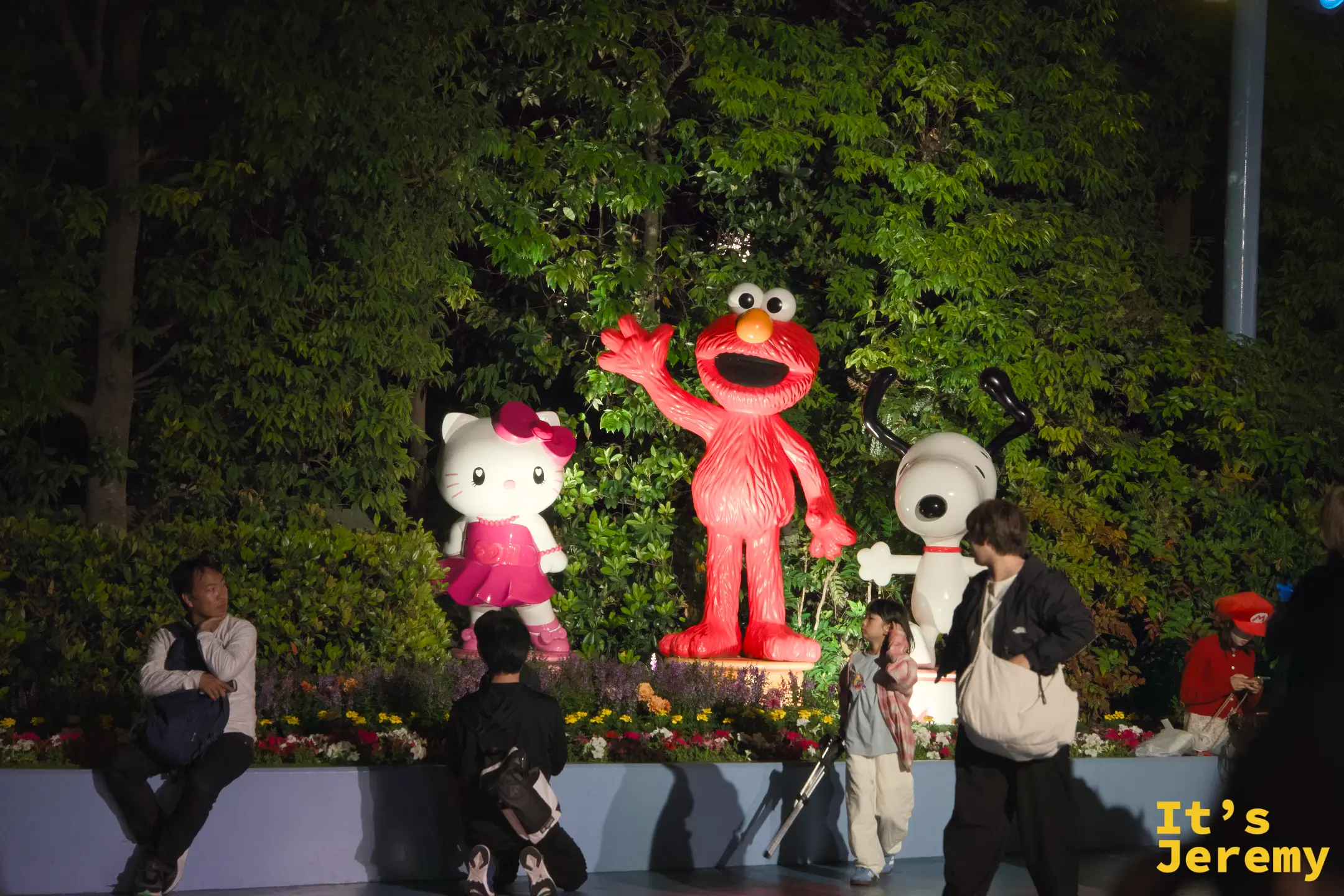 Hello Kitty、Elmo 與 Snoopy 的雕像圍繞在花圃燈光中，在深夜裡靜靜等著與每一個訪客道別
