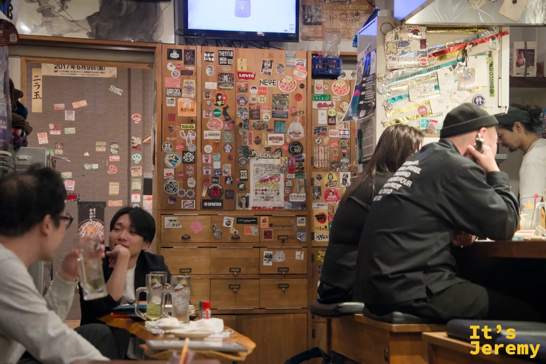 店內全景，座位幾乎坐滿，外國旅客與本地客人比肩而坐，電視開著