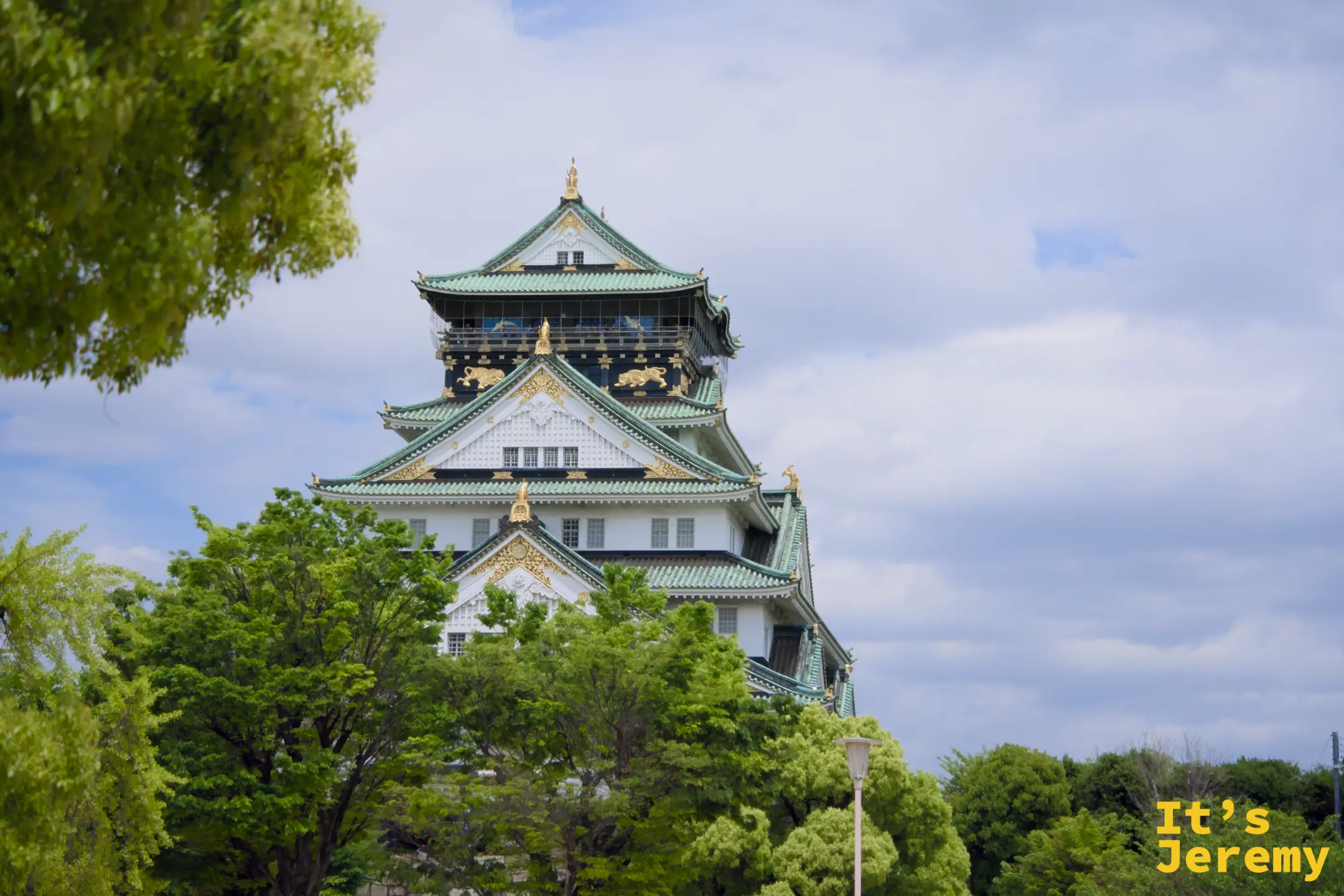 從公園樹叢縫隙看去，翠葉把天守閣頂層框在裡頭