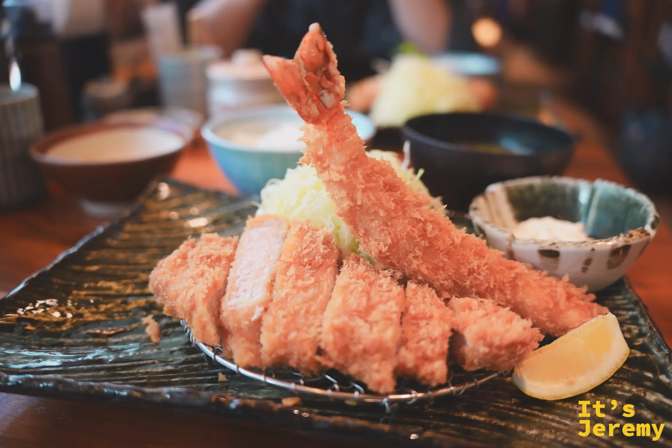 大海老金華ロース套餐：切段炸里肌豬排排列在黑石板上，一隻大蝦炸物豎立其中，旁邊配有芝麻醬小碟和半片檸檬