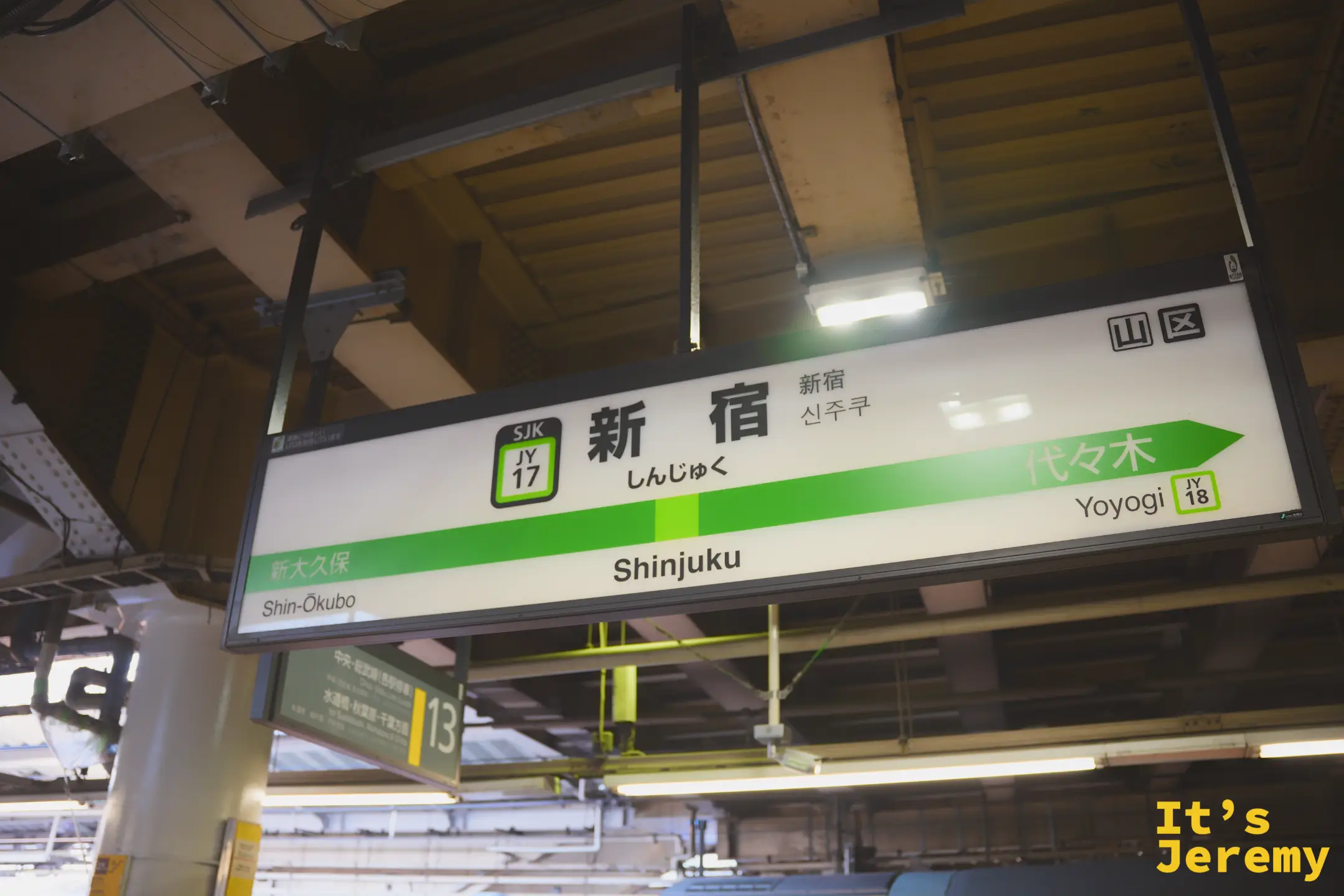 JR 新宿站月台的站名看板，山手線的綠色長條橫貫版面，韓文和英文同時標示著「Shinjuku」