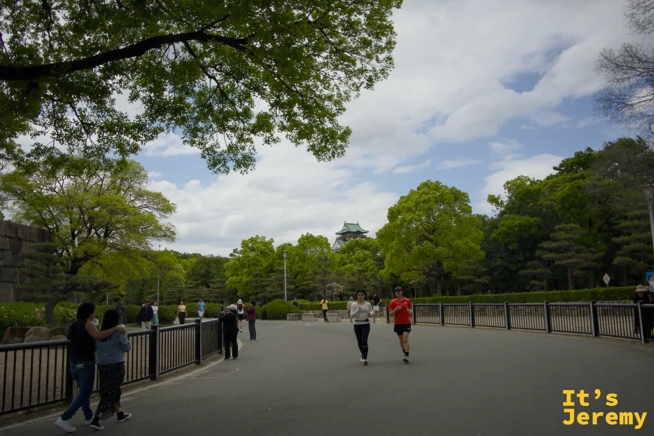 大阪城公園裡，兩名跑者從天守閣背景前跑過，周圍是新綠茂密的大樹