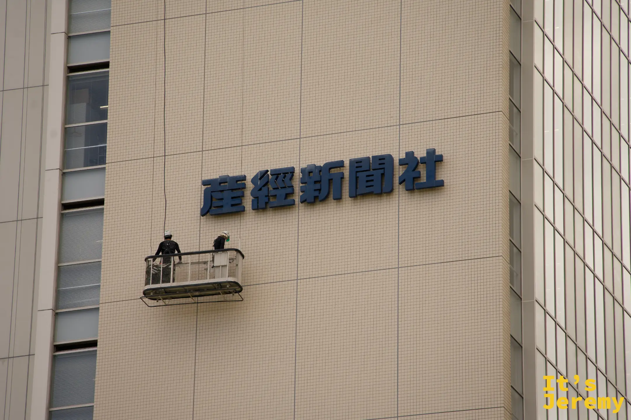 産経新聞社大樓外牆，兩名工人站在吊籠上進行外牆維修作業