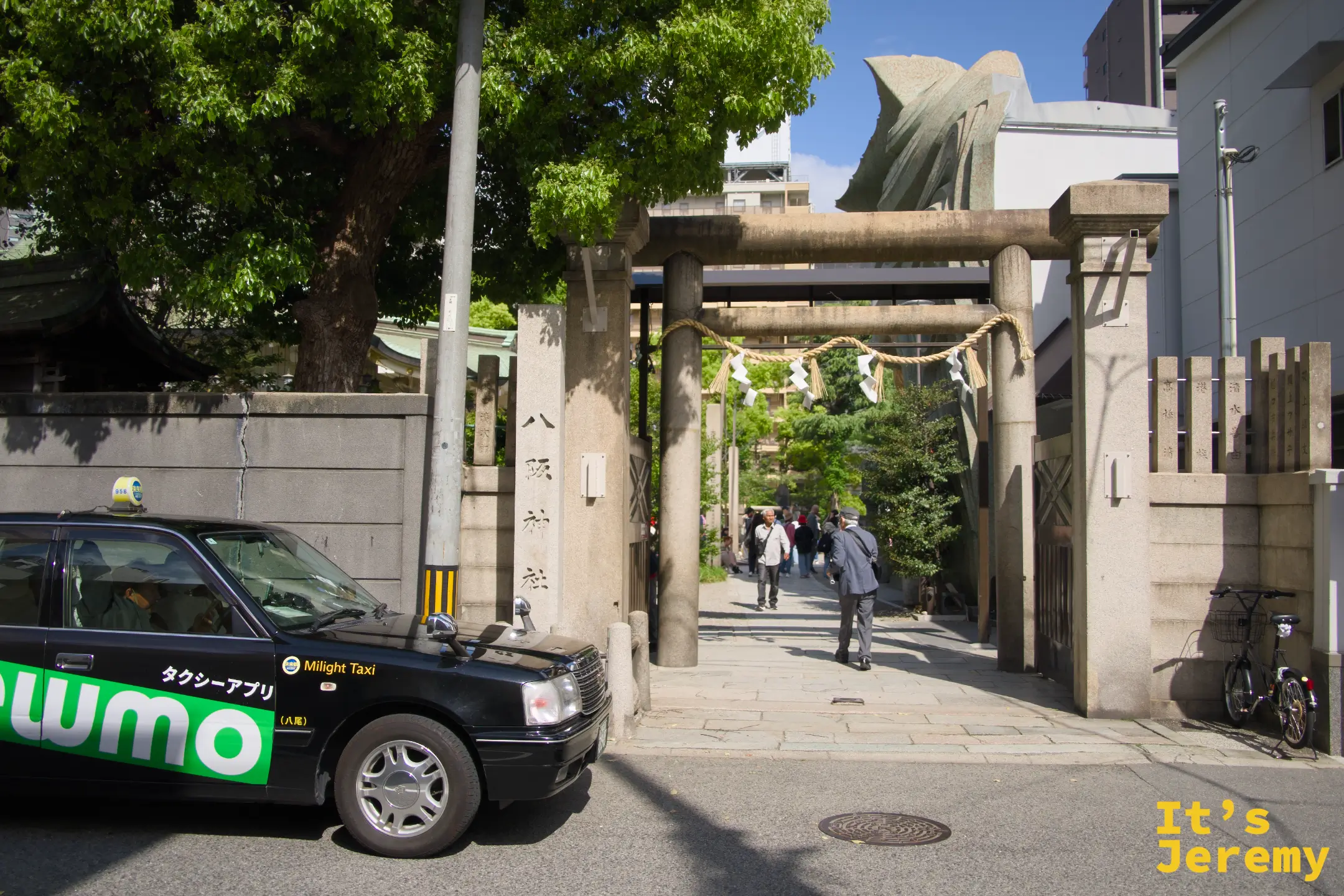 神社鳥居入口，石柱刻有「八阪神社」字樣，背景隱約可見獅子頭建築