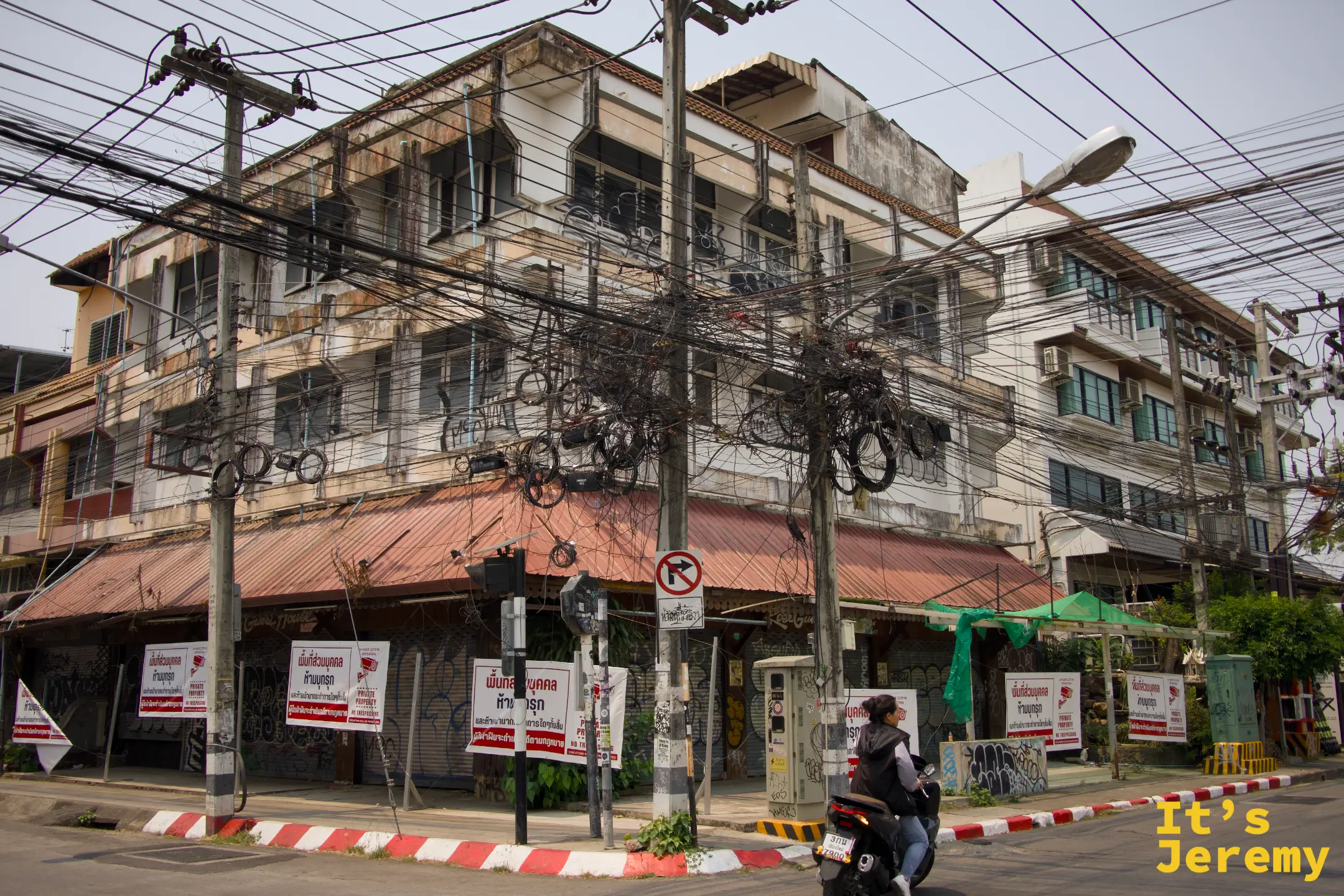 清邁街角老舊公寓,外牆上電線如蛛網般交織,路口停靠著機車