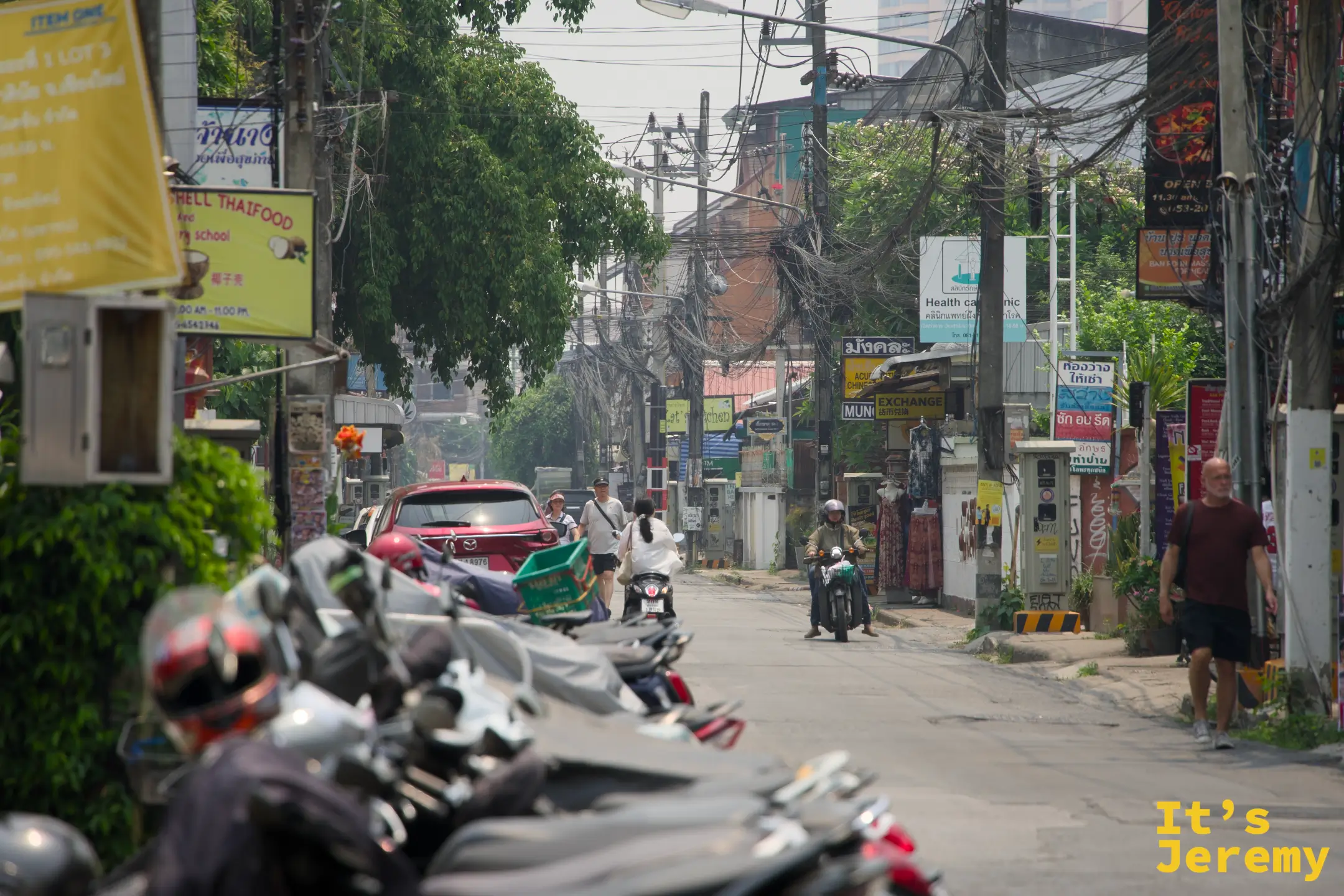 清邁市區街道縱深,前景停滿機車,遠處行人走在店家招牌與電線之間