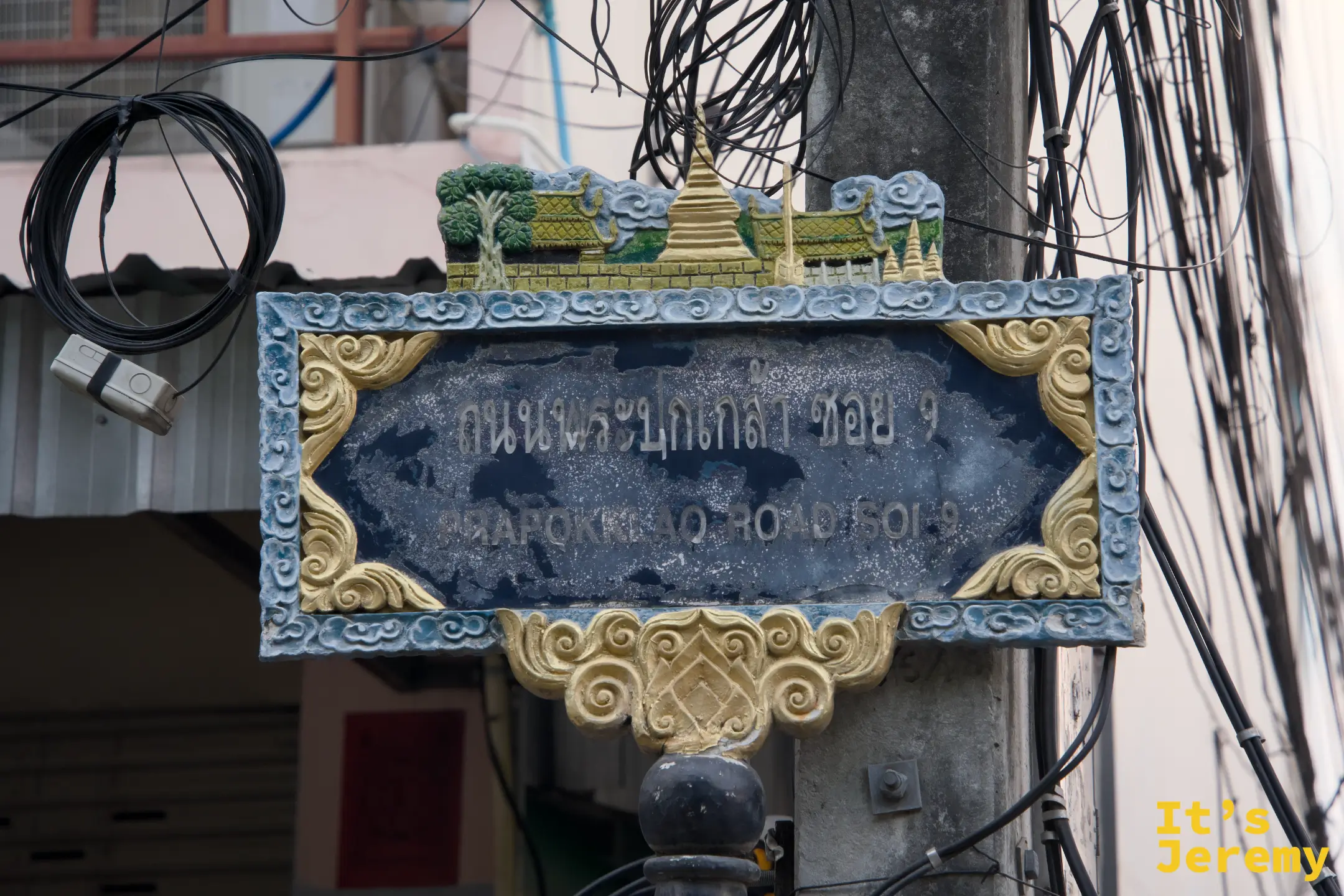 蘭納風格路牌,藍底金框卷草紋,頂端是蘭納寺廟建築群浮雕,寫著 Prapokklao Road Soi 9