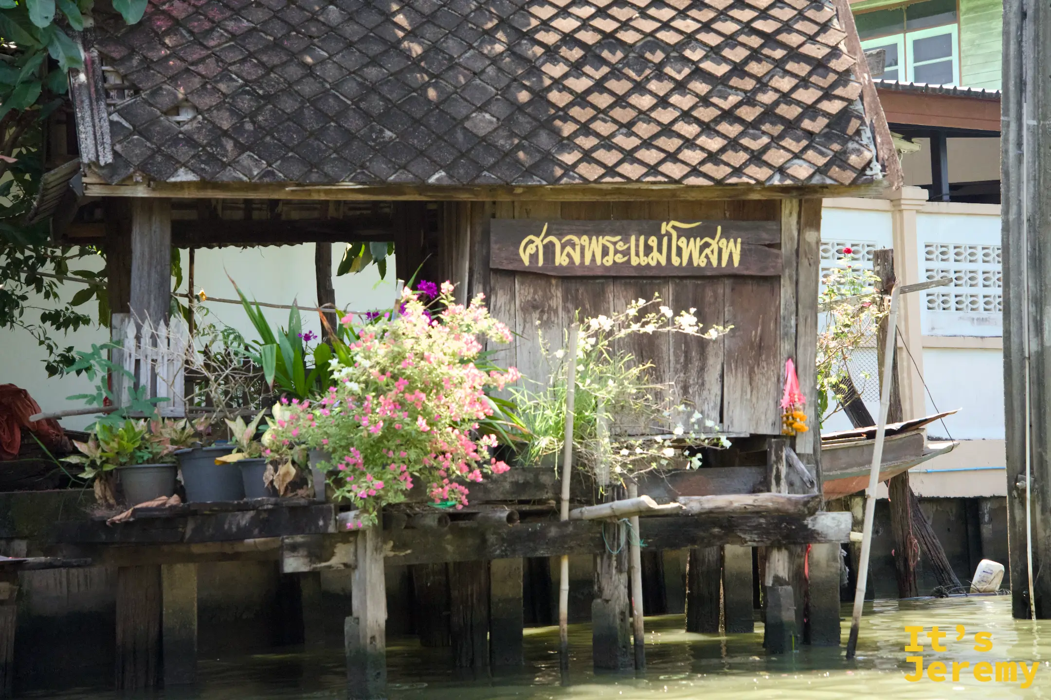 運河旁掛著「ศาลพระแม่โพสพ」（米神祠）小木牌的高腳神龕，旁邊一艘小木船靜靜停著