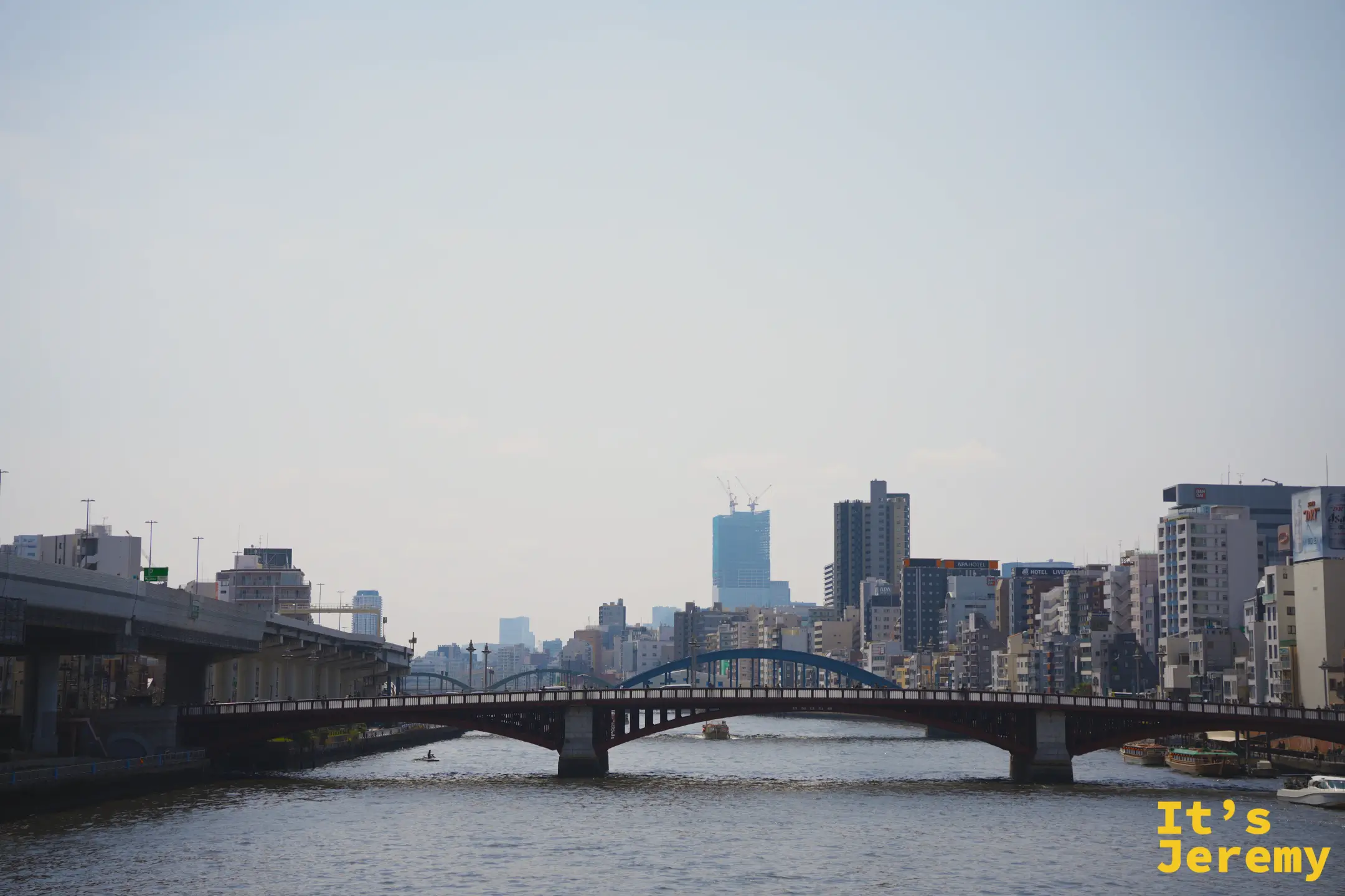 隅田川上的紅色拱橋橫跨河面，背後是霧霾中的東京市區天際線