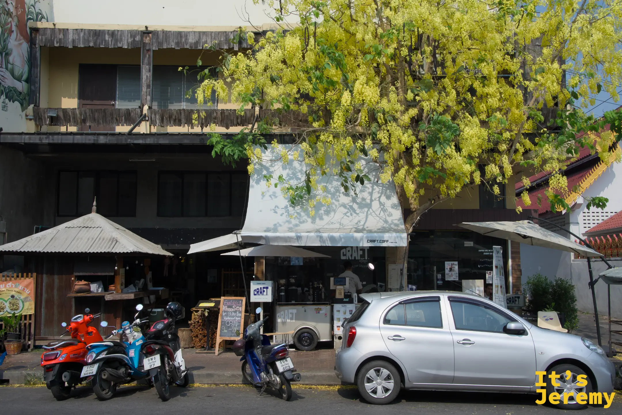 清邁古城早晨的街道，一家咖啡廳靜靜開著門，黃色花樹冠就在招牌上方