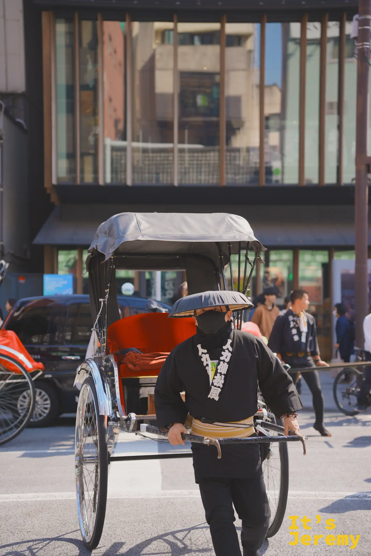 人力車師傅穿著黑色短褂站在車旁，背景帶出淺草街道的環境