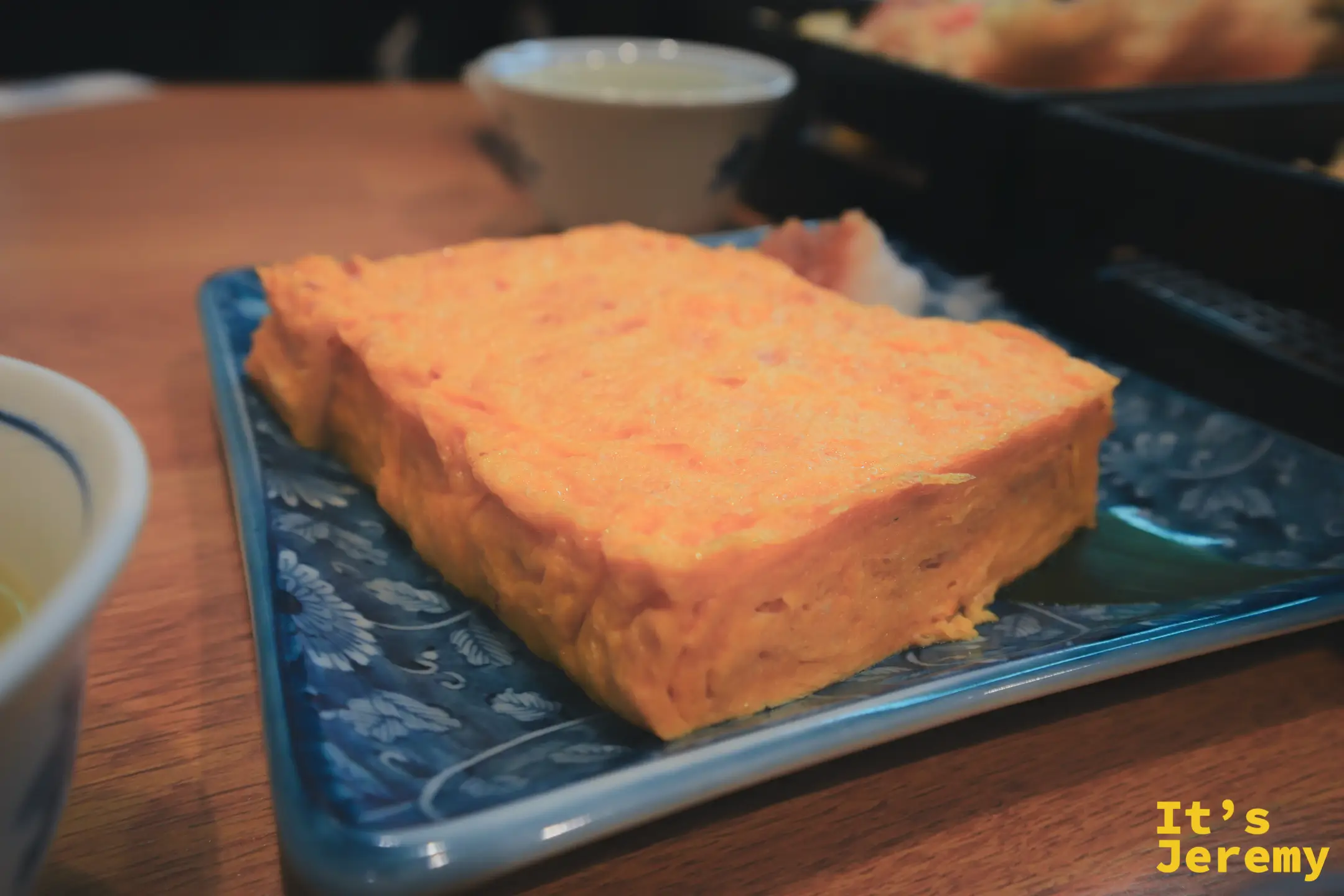 葵丸進玉子燒特寫，橘黃飽滿的厚蛋放在藍白花紋陶盤上，色澤均勻