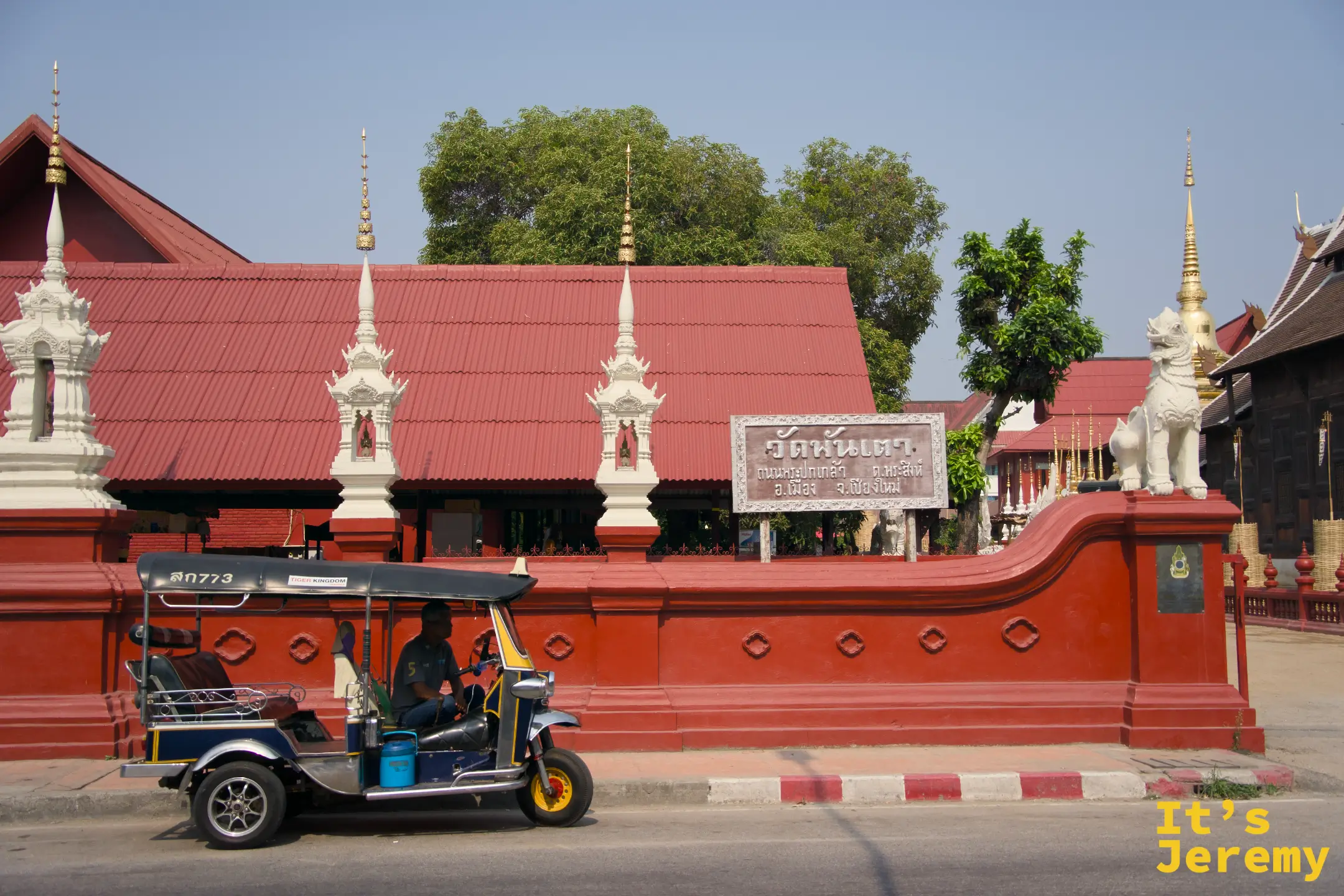 清邁盼道寺 Wat Phan Tao 入口朱紅院牆，嘟嘟車停在外側，白色獅子守護像佇立兩端