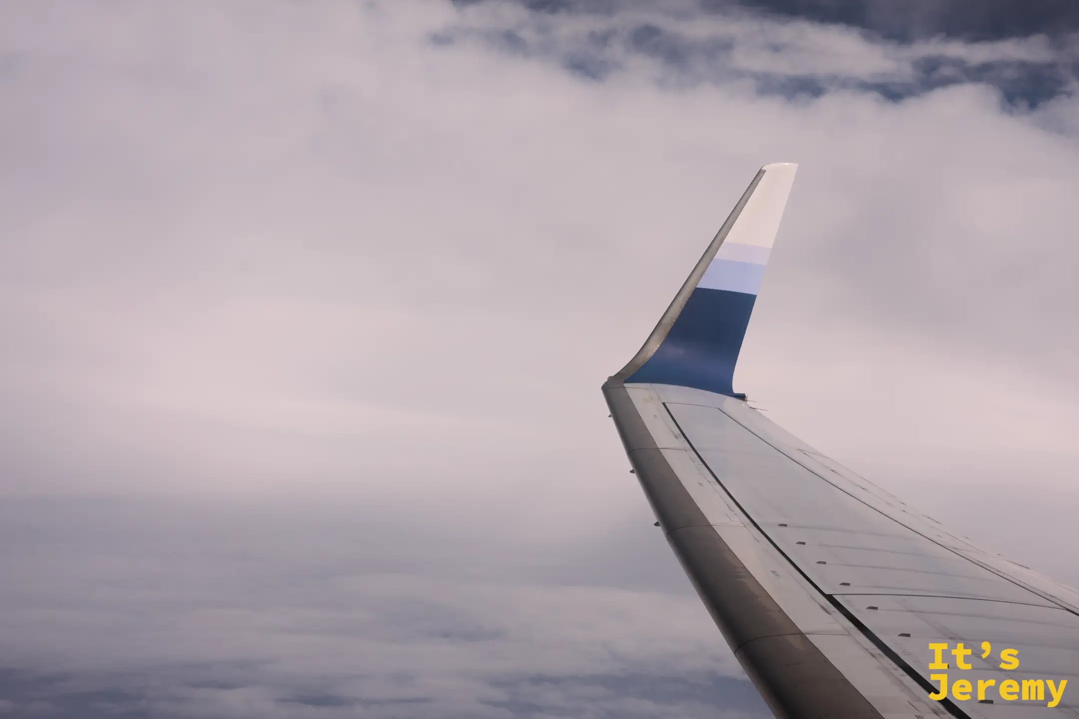 飛機機翼在厚厚的雲層上方劃過，機翼翼尖帶藍白漸層塗裝