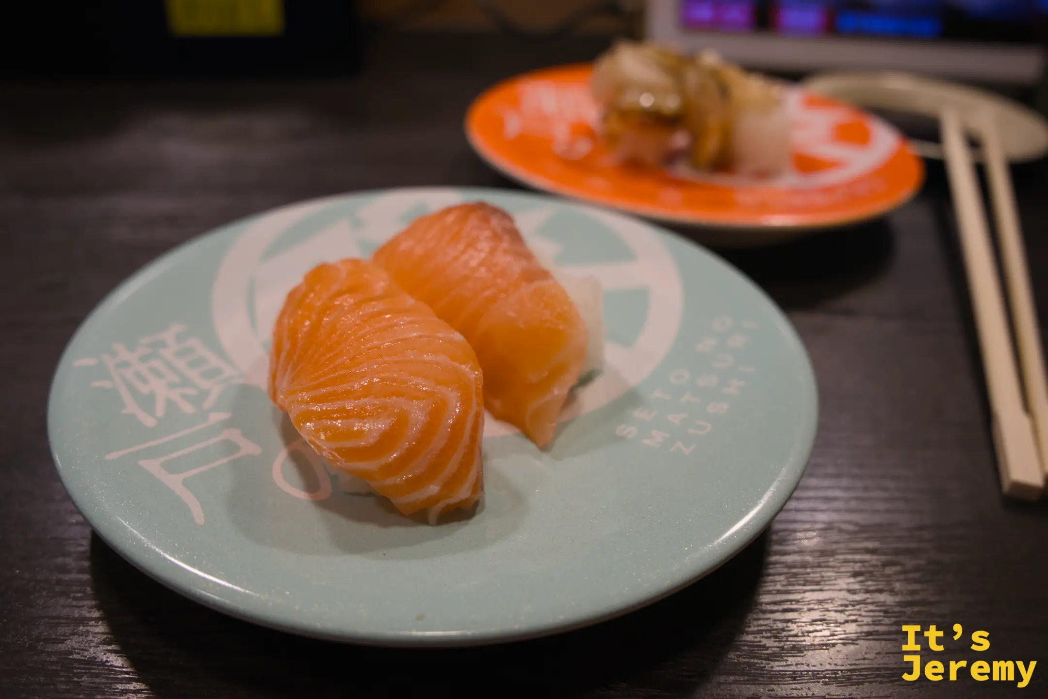 迴轉壽司盤上兩貫鮭魚握壽司，魚肉橙色紋路清晰，盤印「瀬戸」字樣