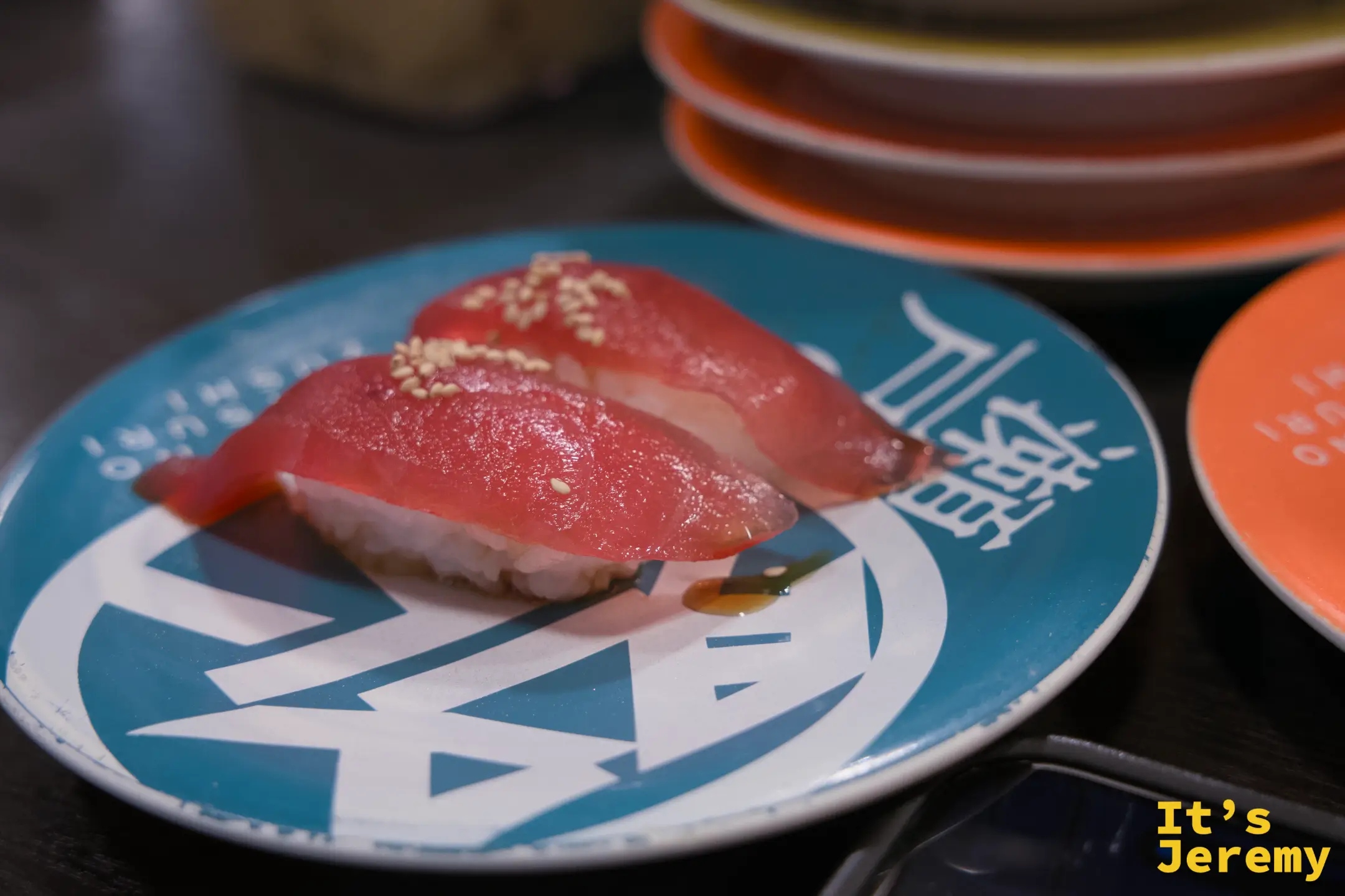 藍綠色盤上兩貫漬鮪魚赤身握壽司，魚肉深紅色澤飽滿，撒芝麻