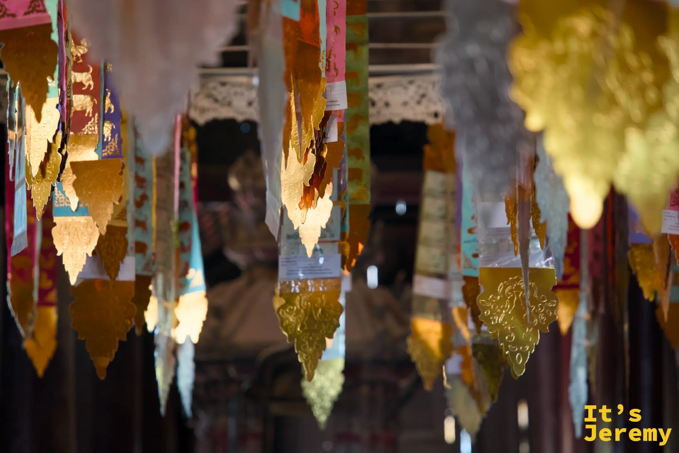 殿頂懸掛的金色、橘色、彩色蘭納供旗（ตุง），在氣流中輕輕搖曳