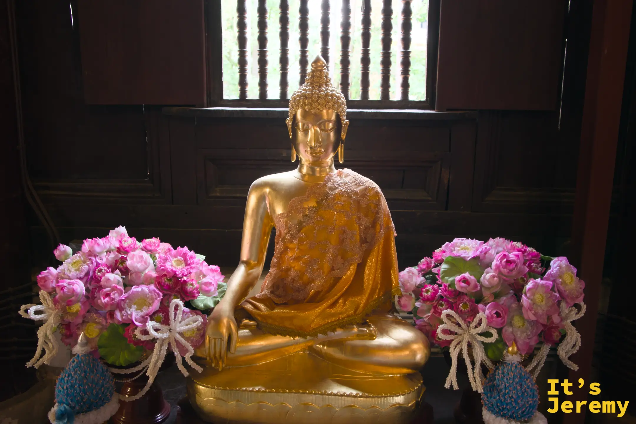 側龕金身坐佛，兩側各擺一束粉色荷花，木格窗逆光勾勒輪廓