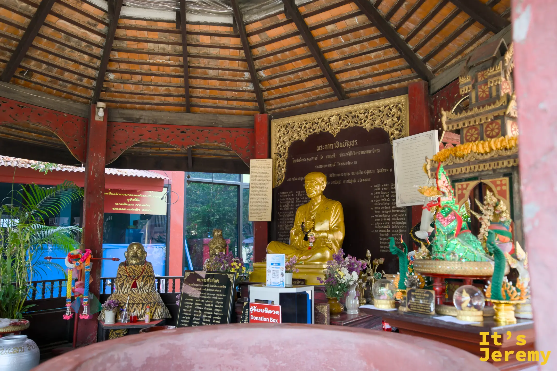 住持紀念亭內，金色高僧坐像居中，四周擺滿信眾供品與器物