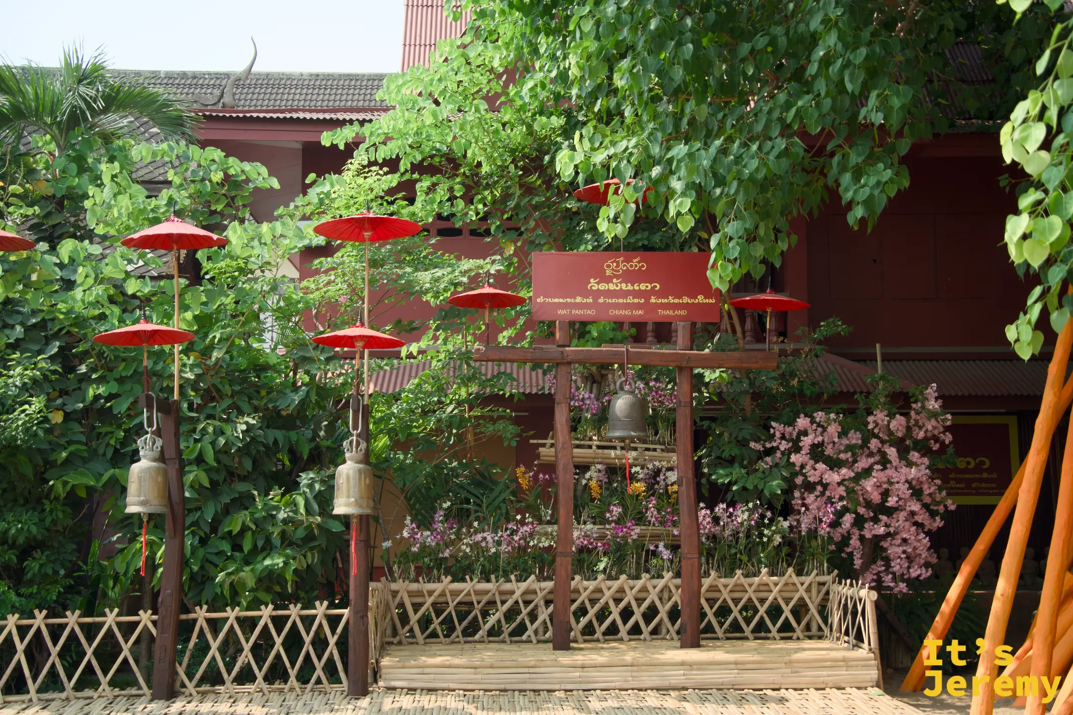 盼道寺入口花園，紅色傘燈、銅鐘排列，竹籬牆上掛著寺廟名牌