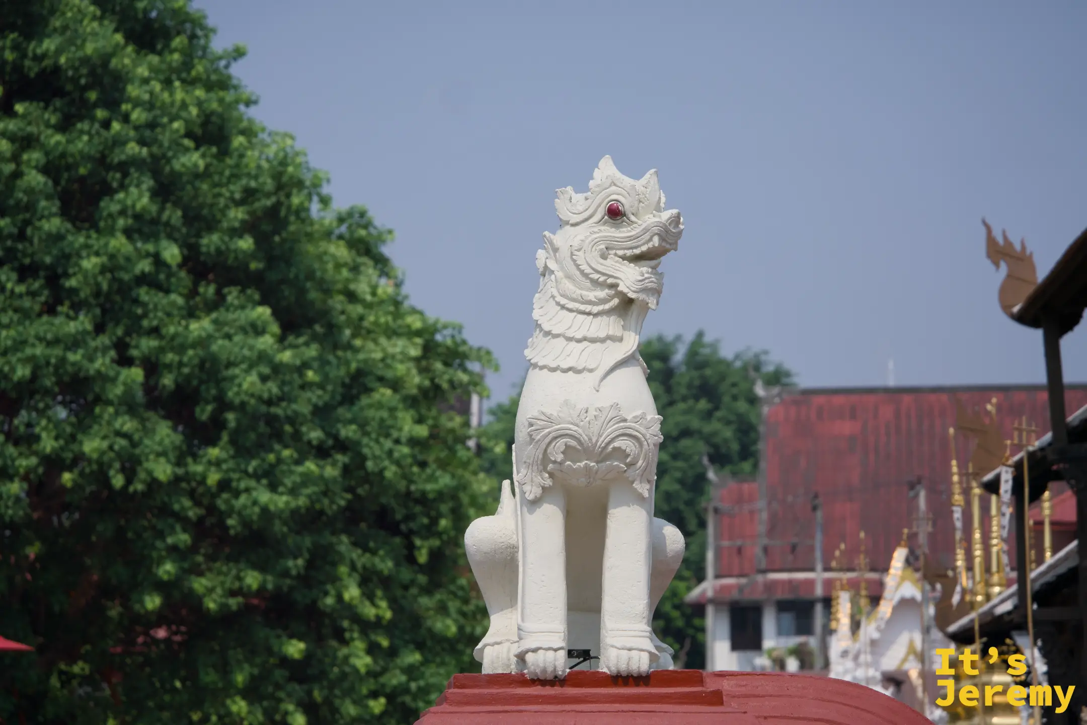 白色獅子守護像（Singha）立於朱紅台座，背景是古城其他寺廟屋頂