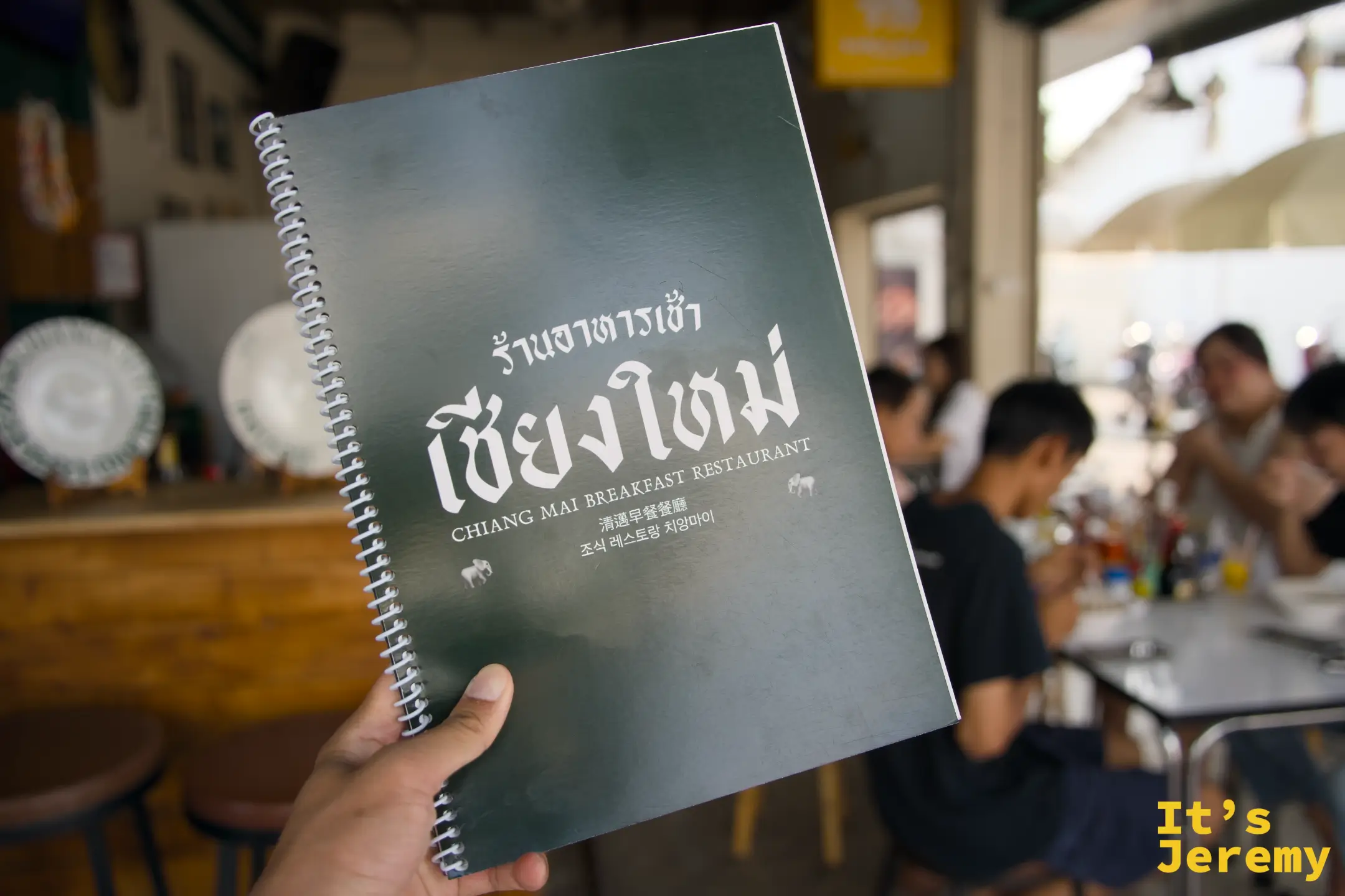 手持 Chiang Mai Breakfast Restaurant 綠色螺旋裝訂菜單本
