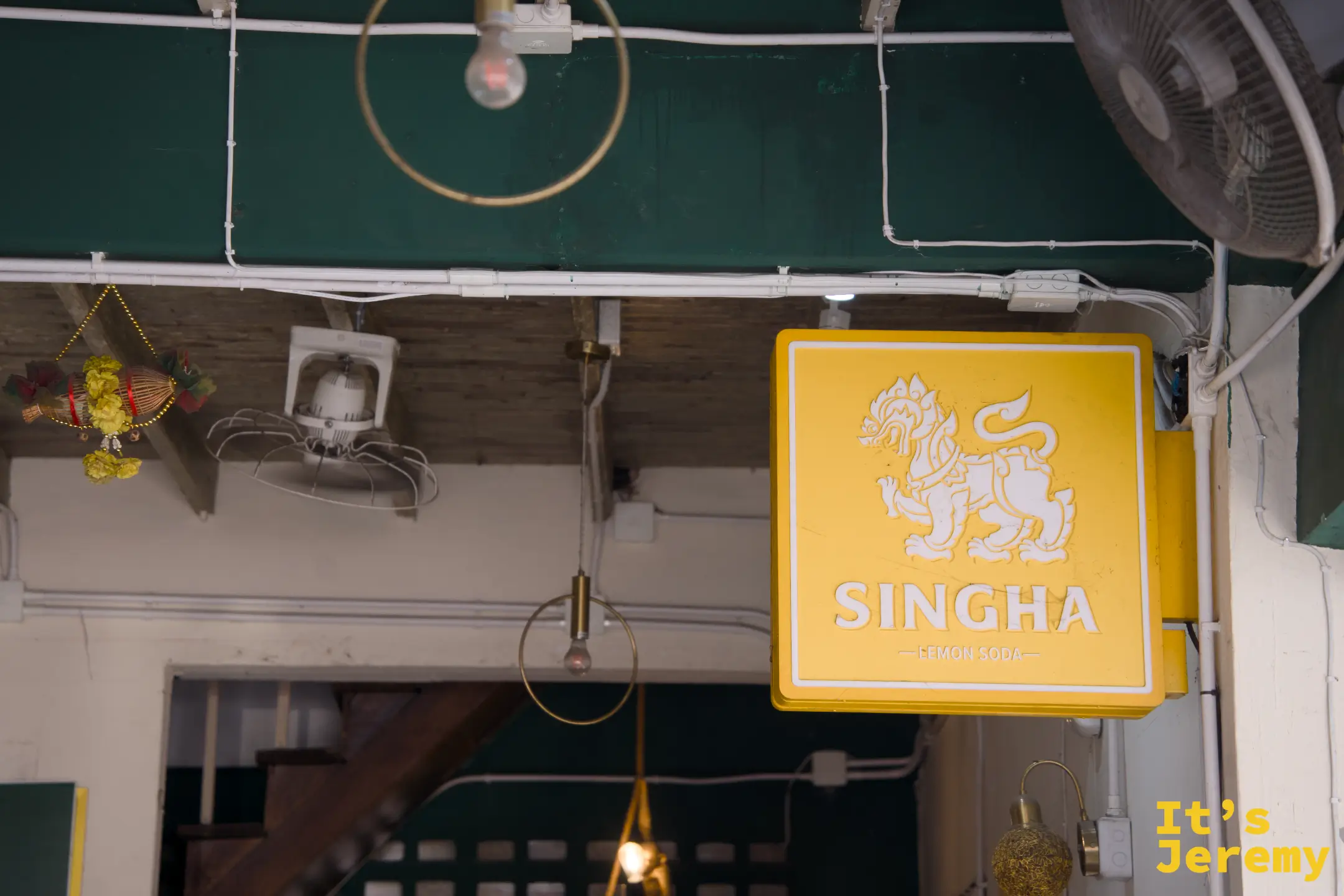 店內 Singha Lemon Soda 黃色燈箱招牌，與綠色天花板對比鮮明