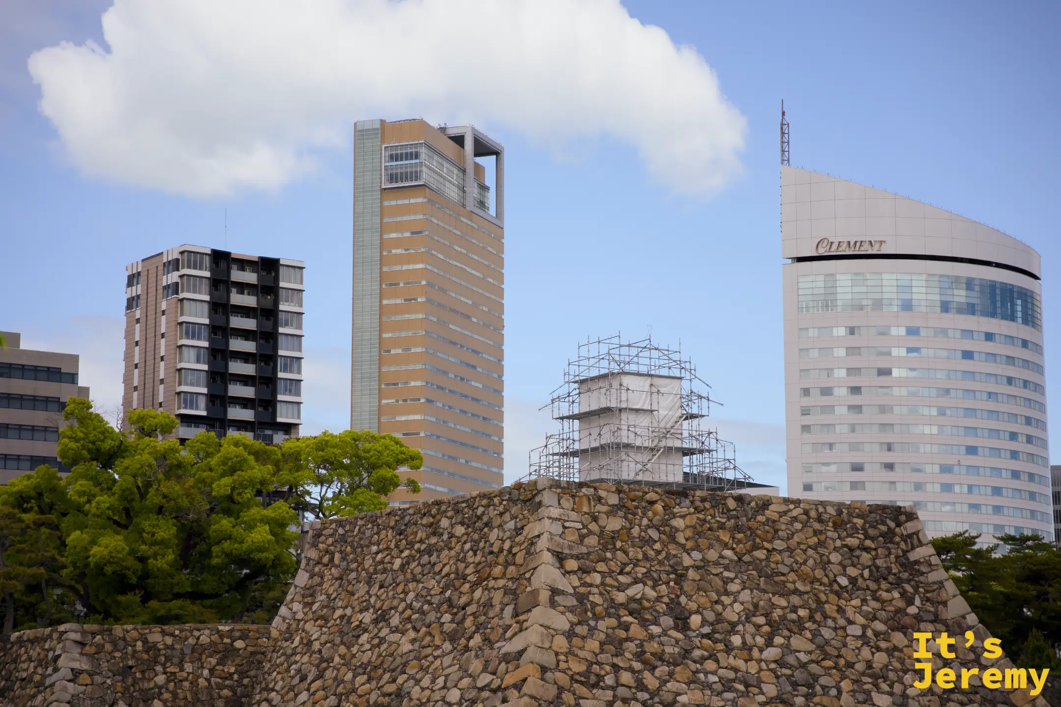 高松城石垣與現代市區建築對比，遠處天守可見修復中的鷹架