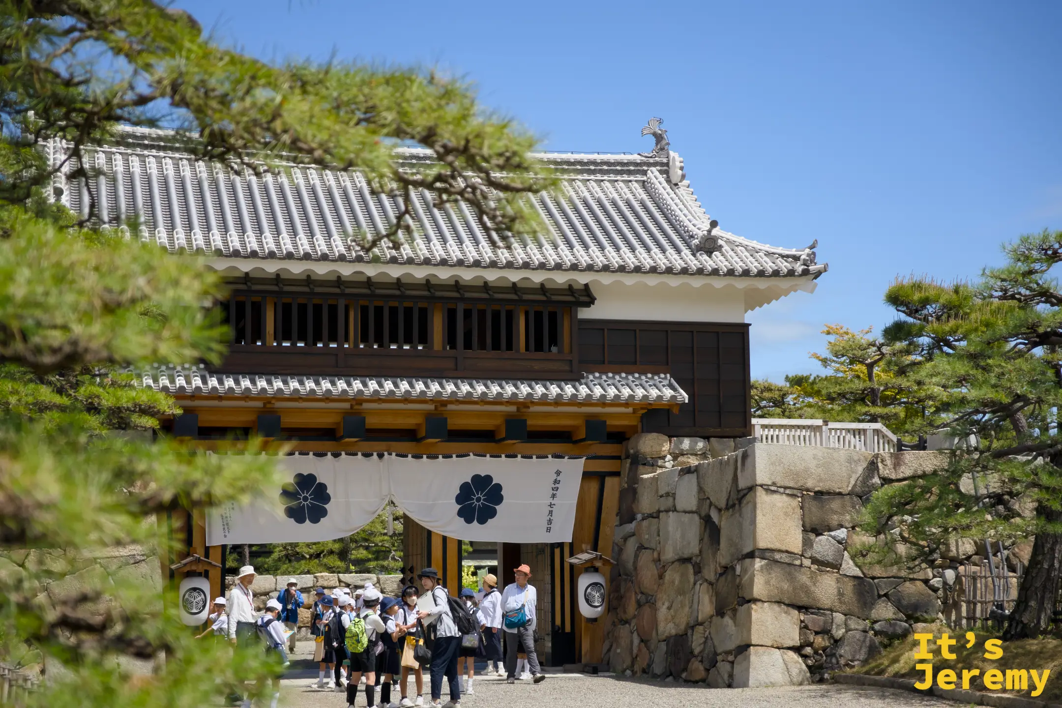 大手門石垣與城門，白色松平家紋幕布掛在門樑，松樹從兩側探出頭