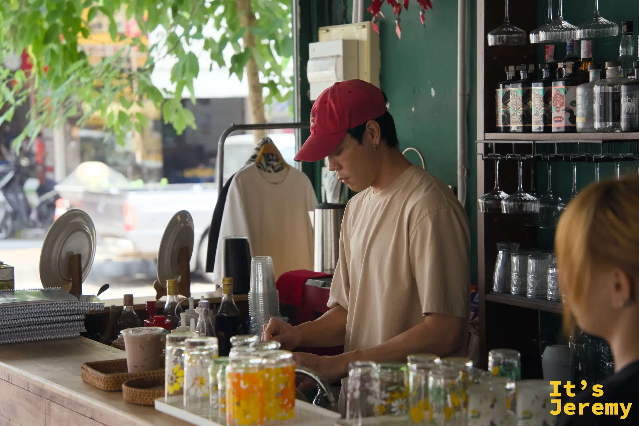 戴紅色棒球帽的店員在吧台後專注備料，背景為飲料架