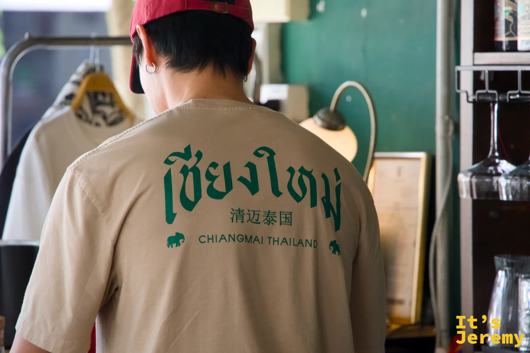 店員戴紅色棒球帽，背對鏡頭，T-shirt 上印有泰文清邁字樣