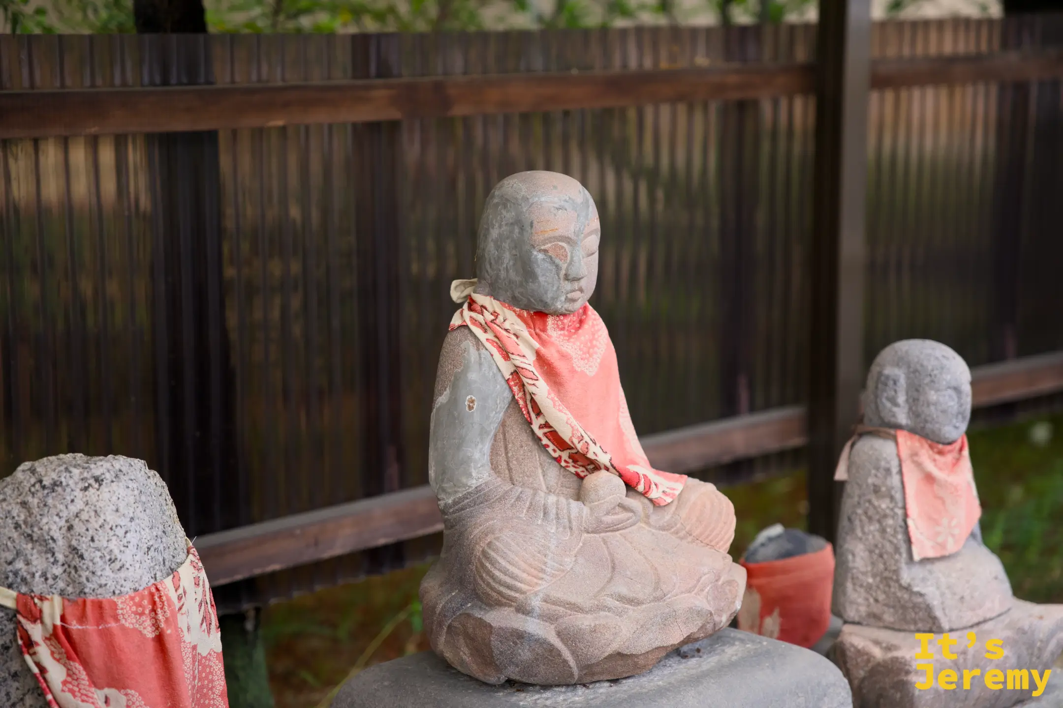 石地藏特寫，中間那尊身著紅白紋路圍裙的地藏面容古樸沉靜，頭頂微微向下