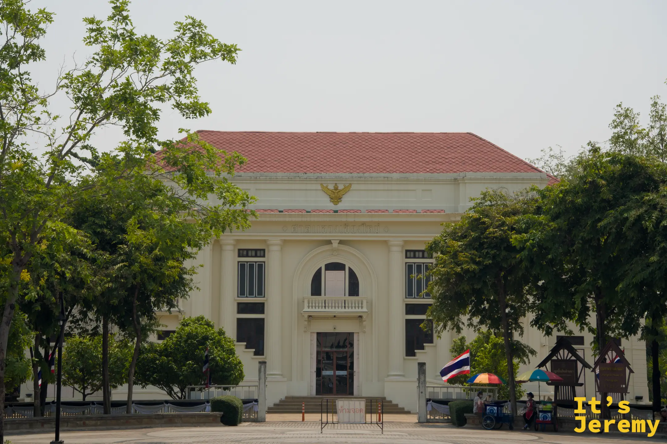 清邁市立藝術文化中心建築全景，透過行道樹望去，歐式立面與橘紅屋瓦在陽光下對比鮮明